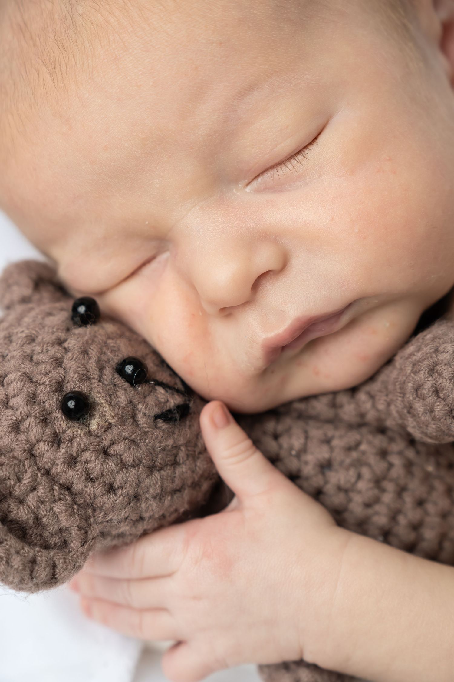 Peaceful newborn baby sleeping while holding a brown crocheted teddy bear, close-up portrait photography.