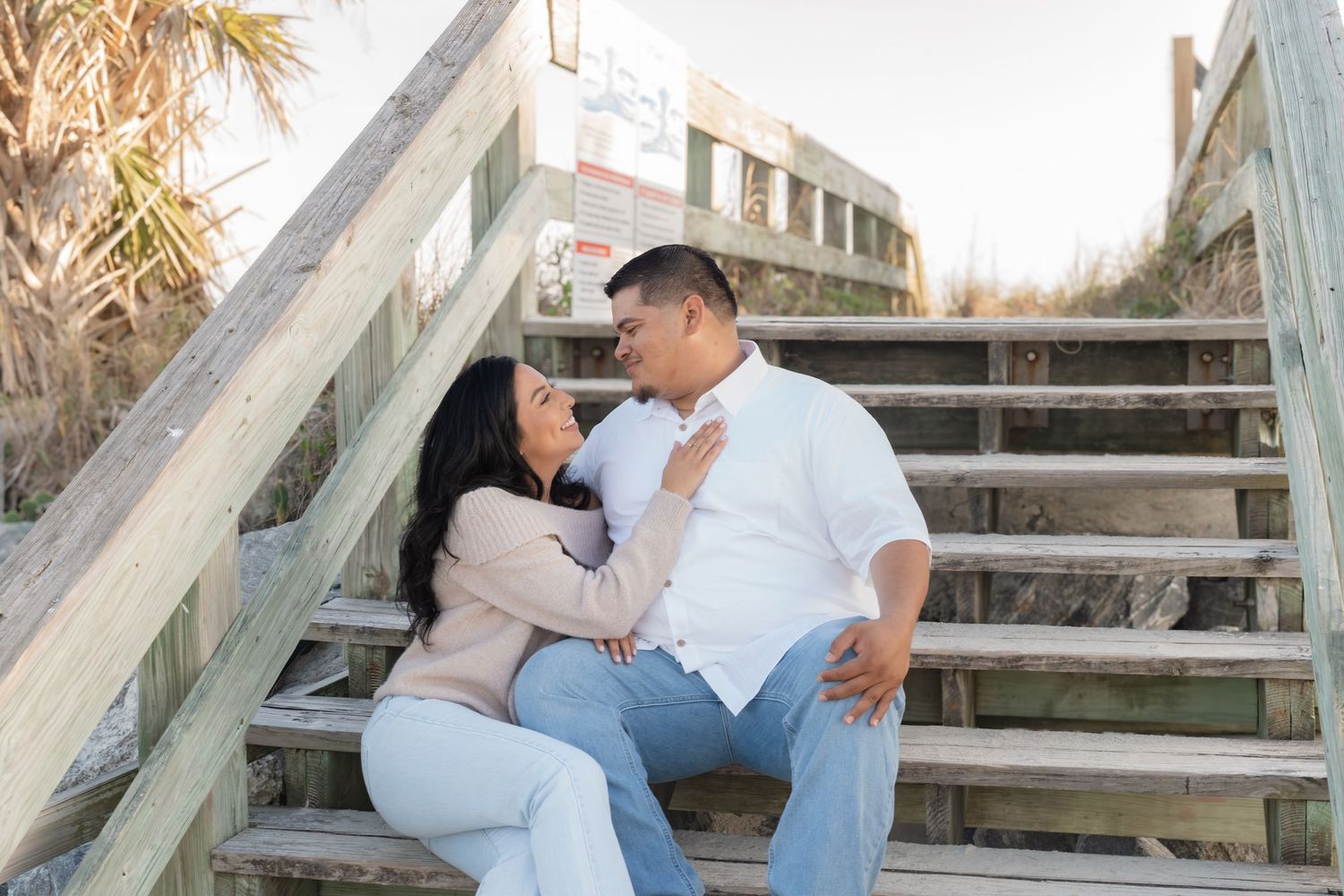 Couple sitting closely on wooden beach stairs, gazing lovingly at each other.