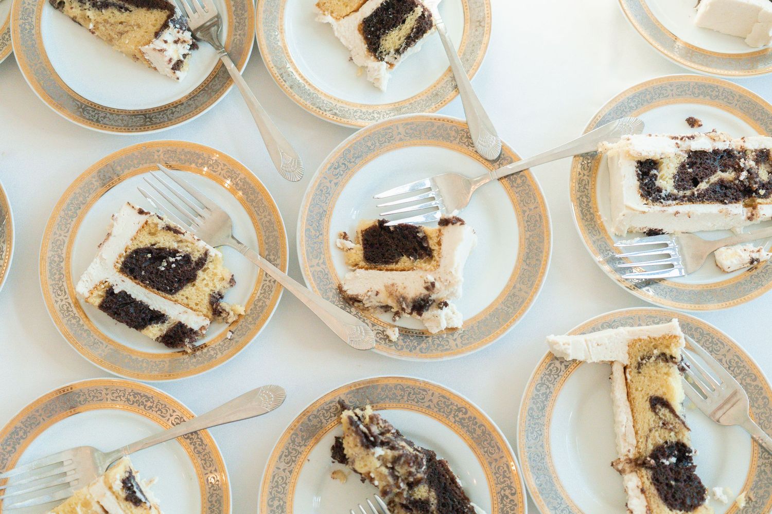 Multiple plates of chocolate and vanilla wedding cake slices with forks on elegant gold-rimmed china plates.