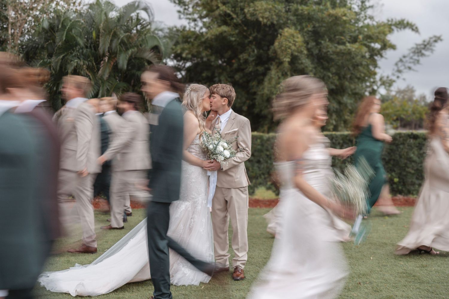 Bride and groom kissing while wedding party moves around them in a motion blur photo.