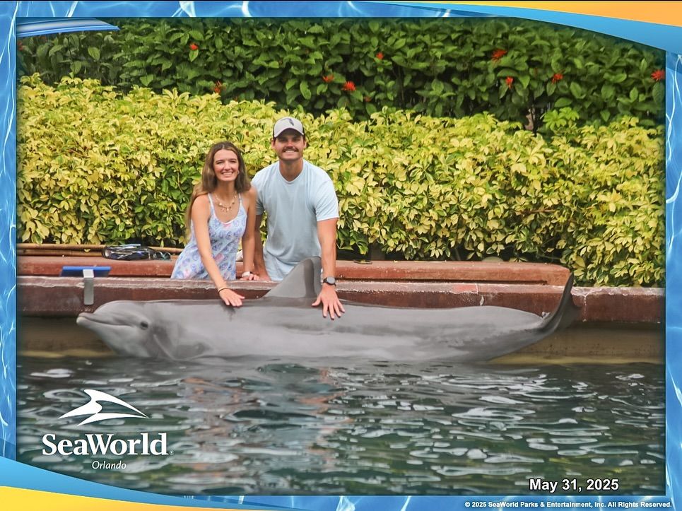 Couple smiles beside a dolphin poolside at SeaWorld Orlando on May 31 2025.