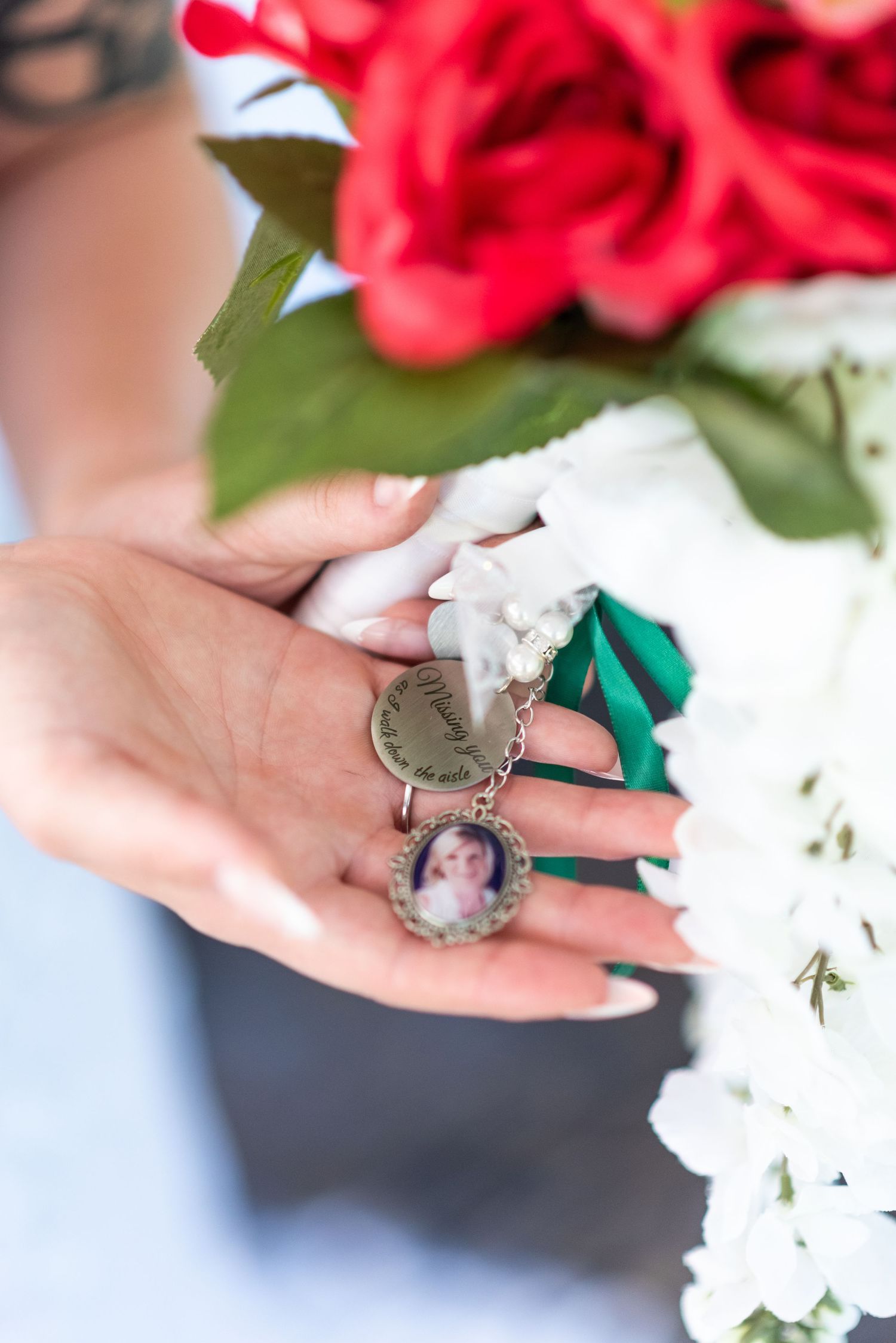 Bride holds a memorial locket charm with photo attached to her bridal bouquet of red and white flowers.