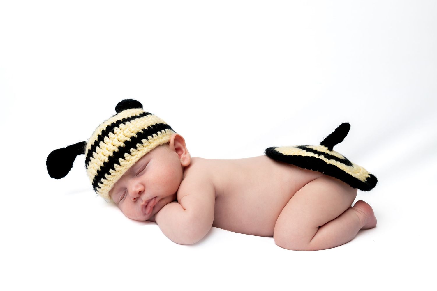 Sleeping newborn baby wearing a cute crocheted black and yellow bumblebee hat and diaper cover costume.