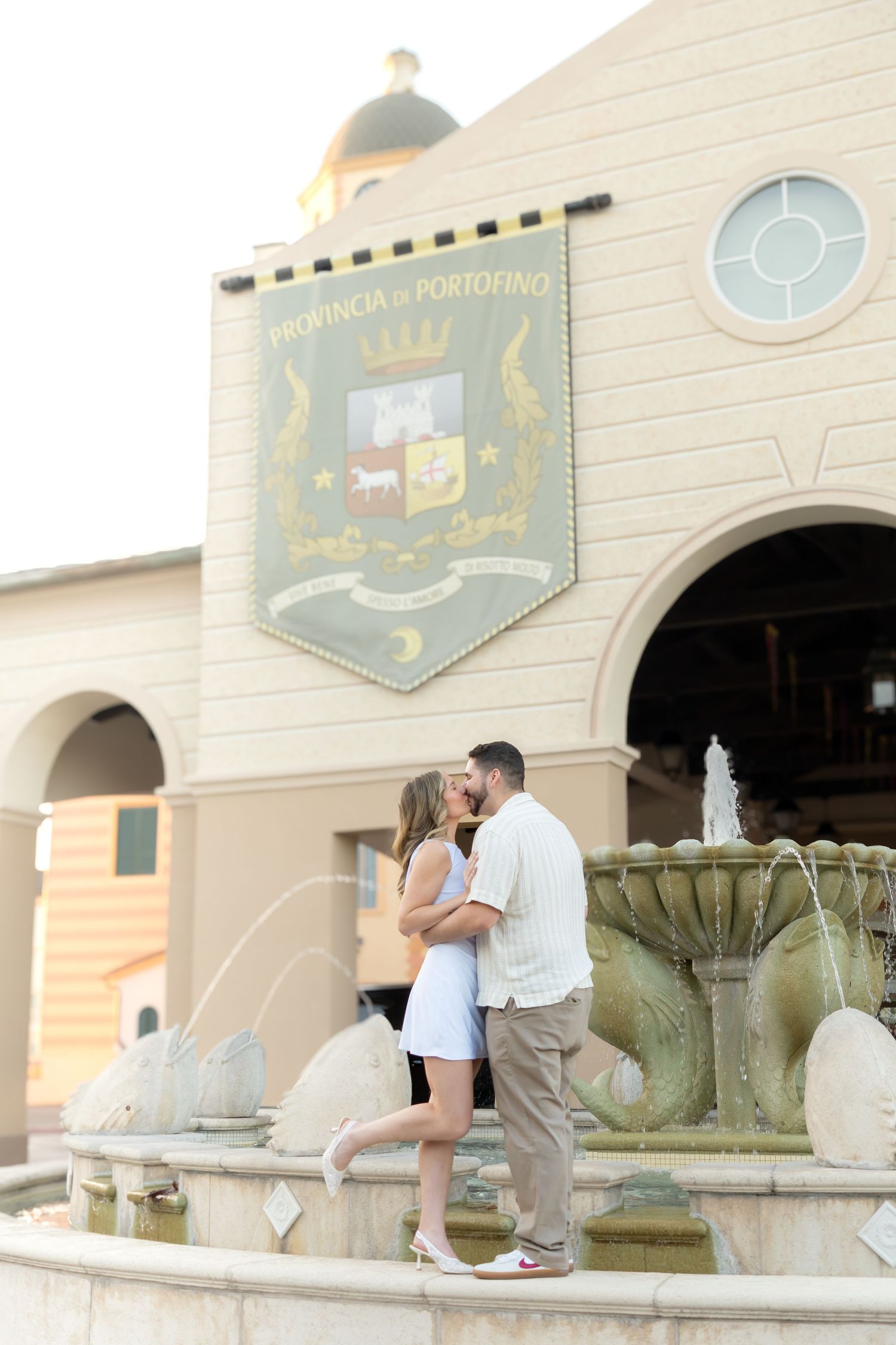 Couple shares intimate moment by decorative fountain outside classic building.