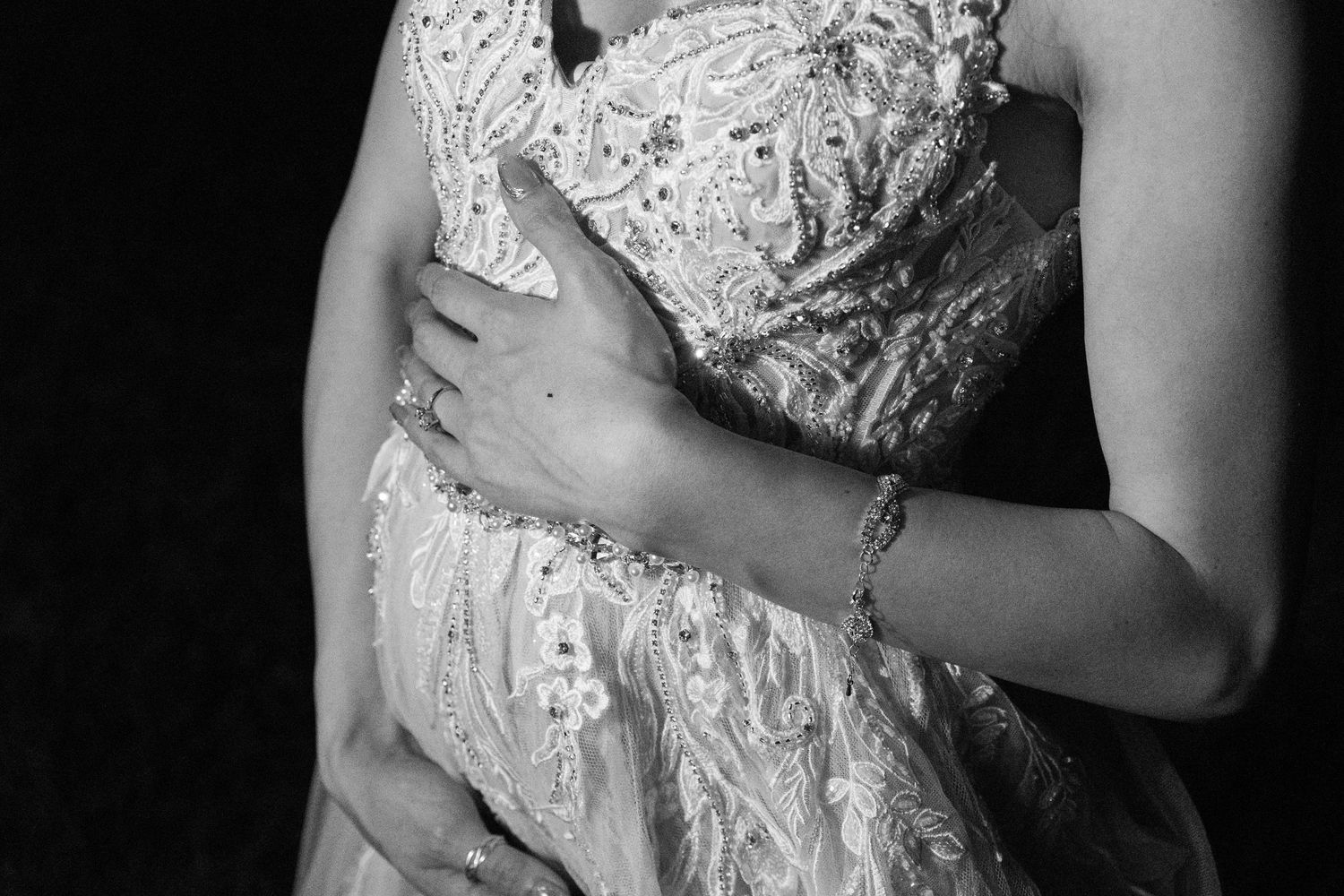 Black and white photo of a pregnant woman in a lace dress, cradling her baby bump with both hands.