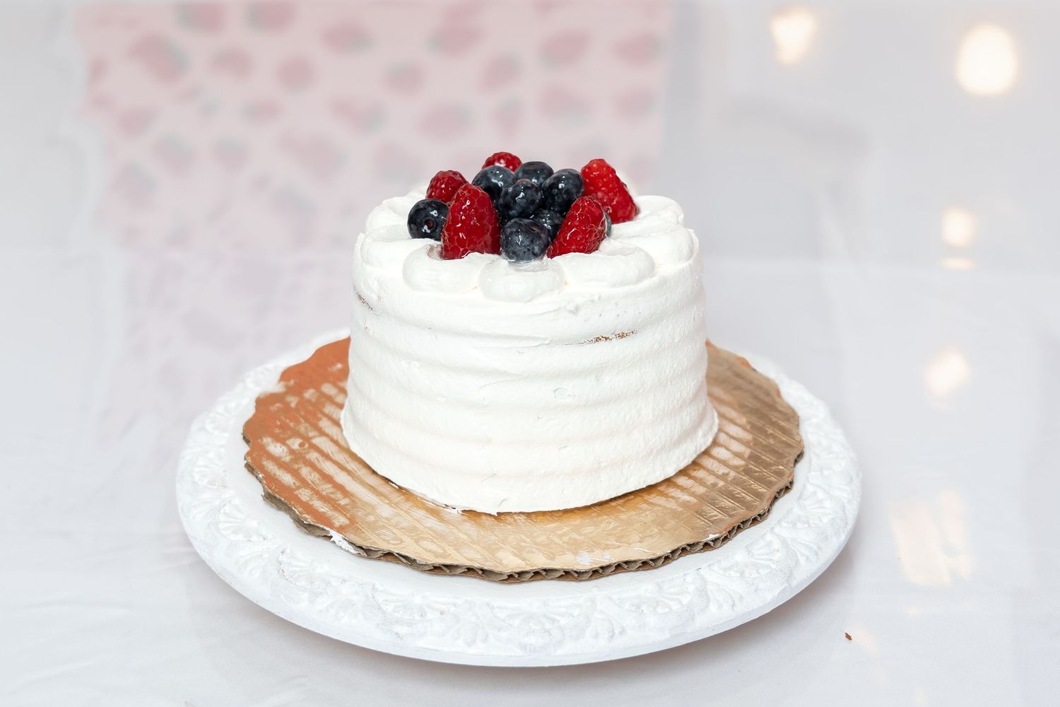 Small white layered smash cake topped with fresh raspberries and blueberries on a decorative white plate.