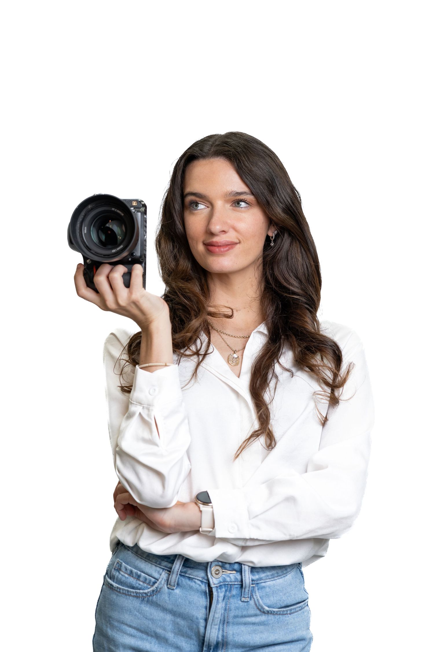 Female photographer holding a professional DSLR camera while looking up thoughtfully, wearing white blouse and jeans.