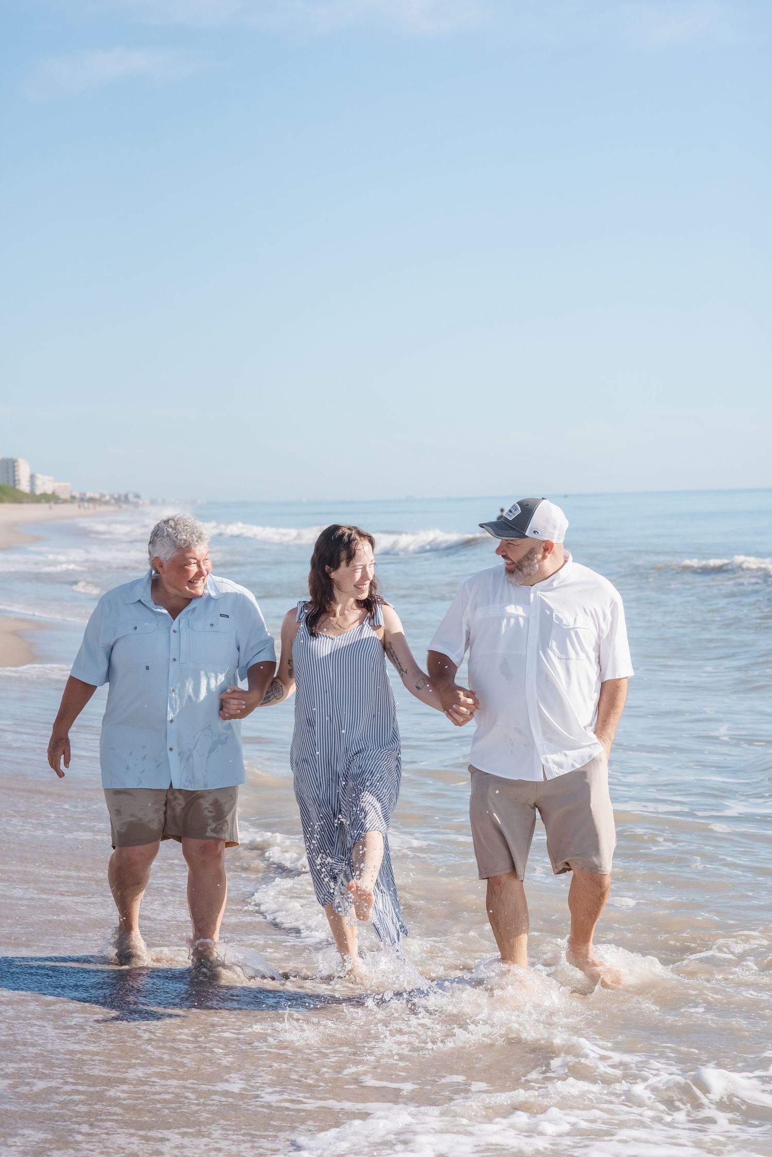 Three people laughing and splashing in ocean waves on a sunny beach day.