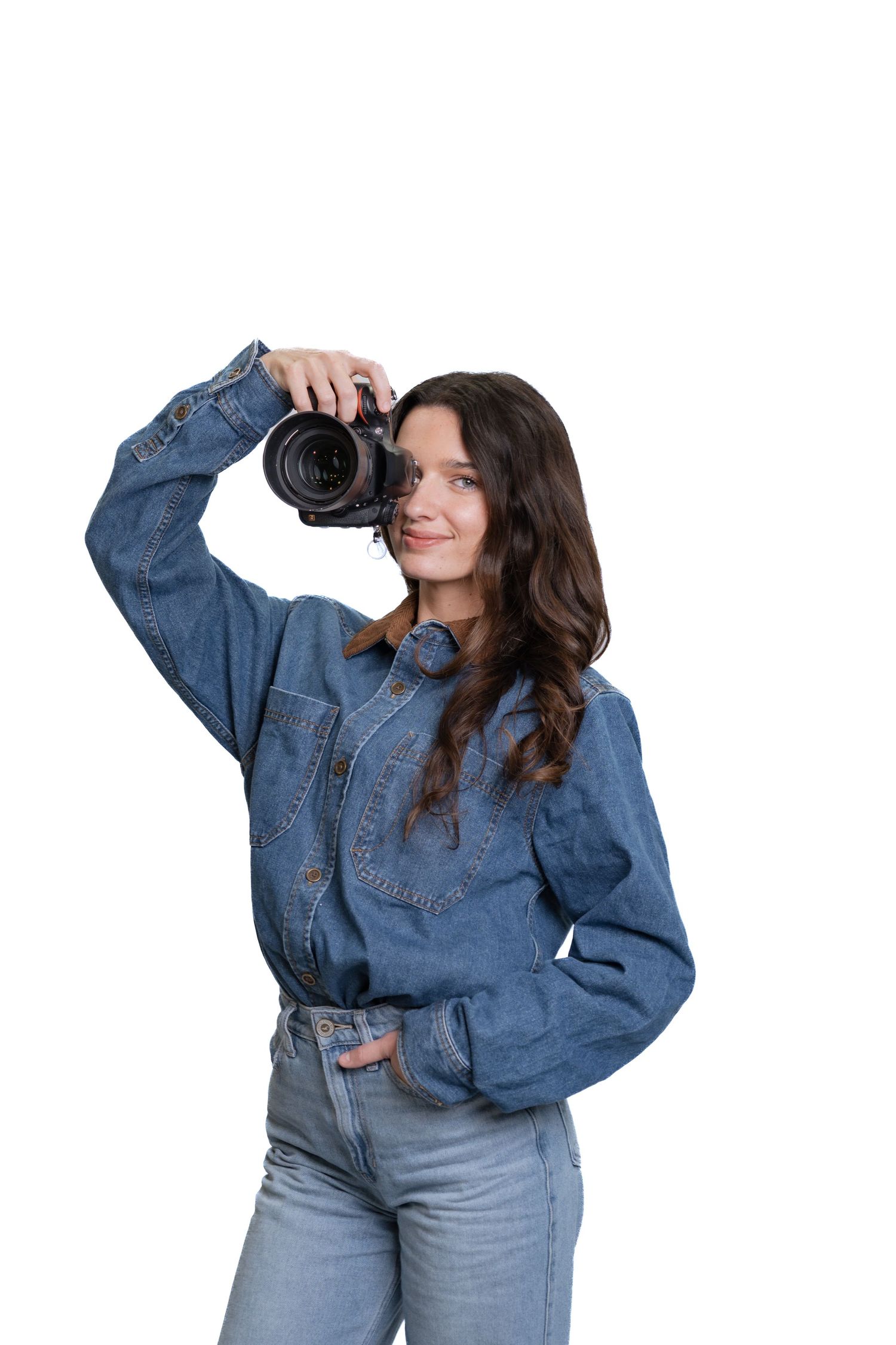 Female photographer in denim shirt raising DSLR camera to take a photo on white background.