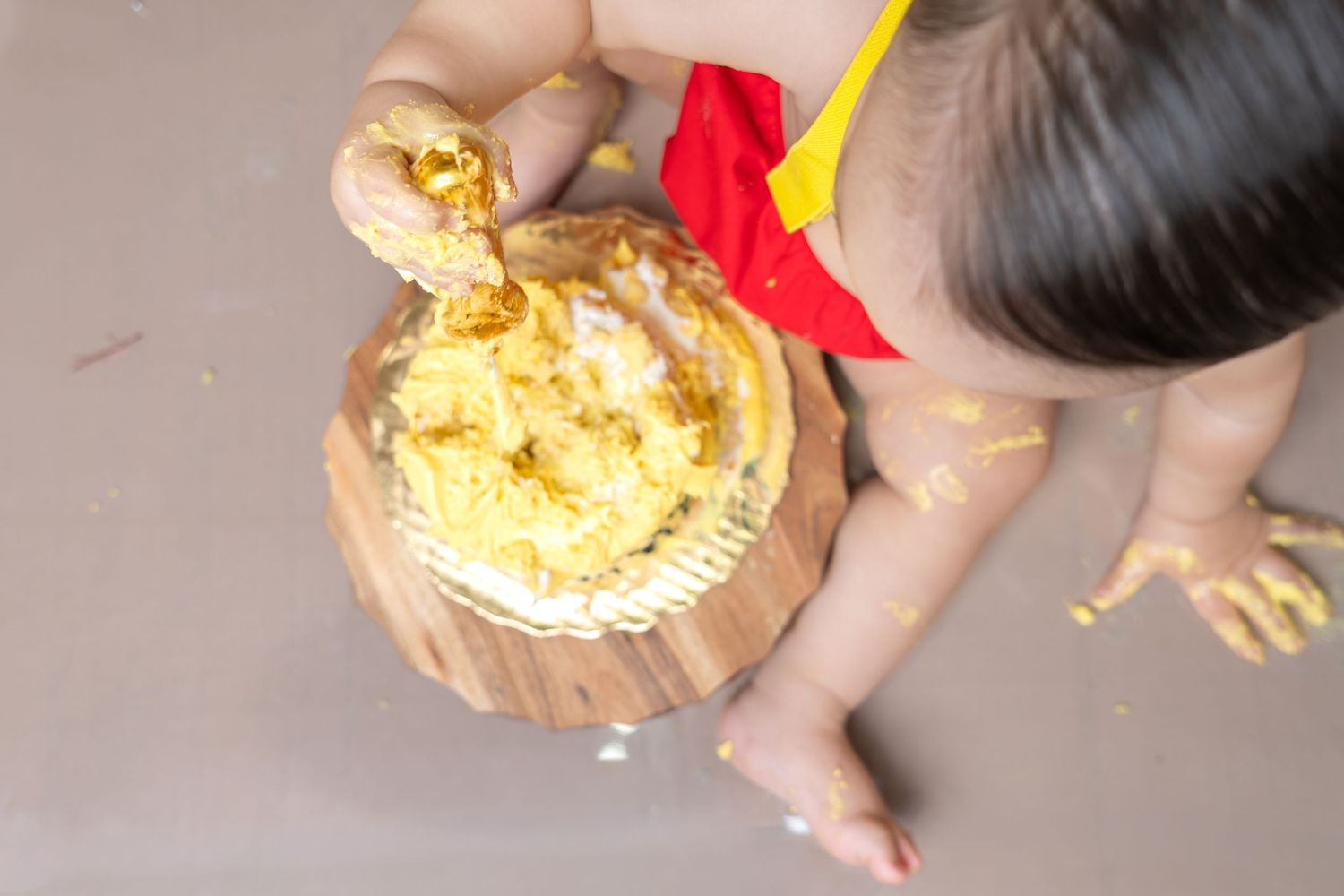 Baby smashing a yellow cake on a wooden board during a first birthday cake smash celebration.