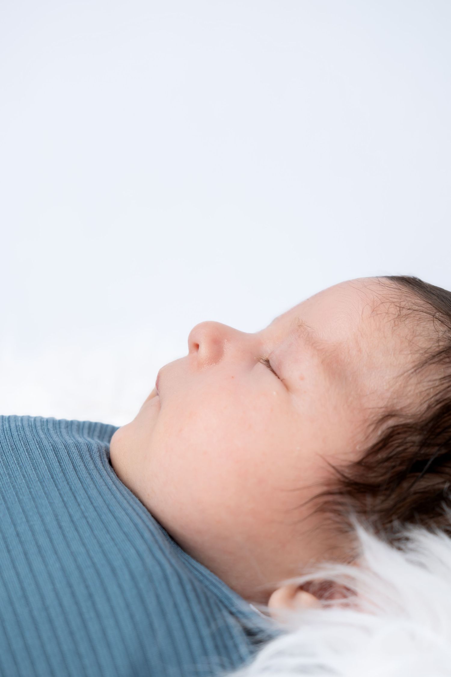Peaceful newborn baby sleeping on a white fluffy blanket wearing a blue ribbed outfit.