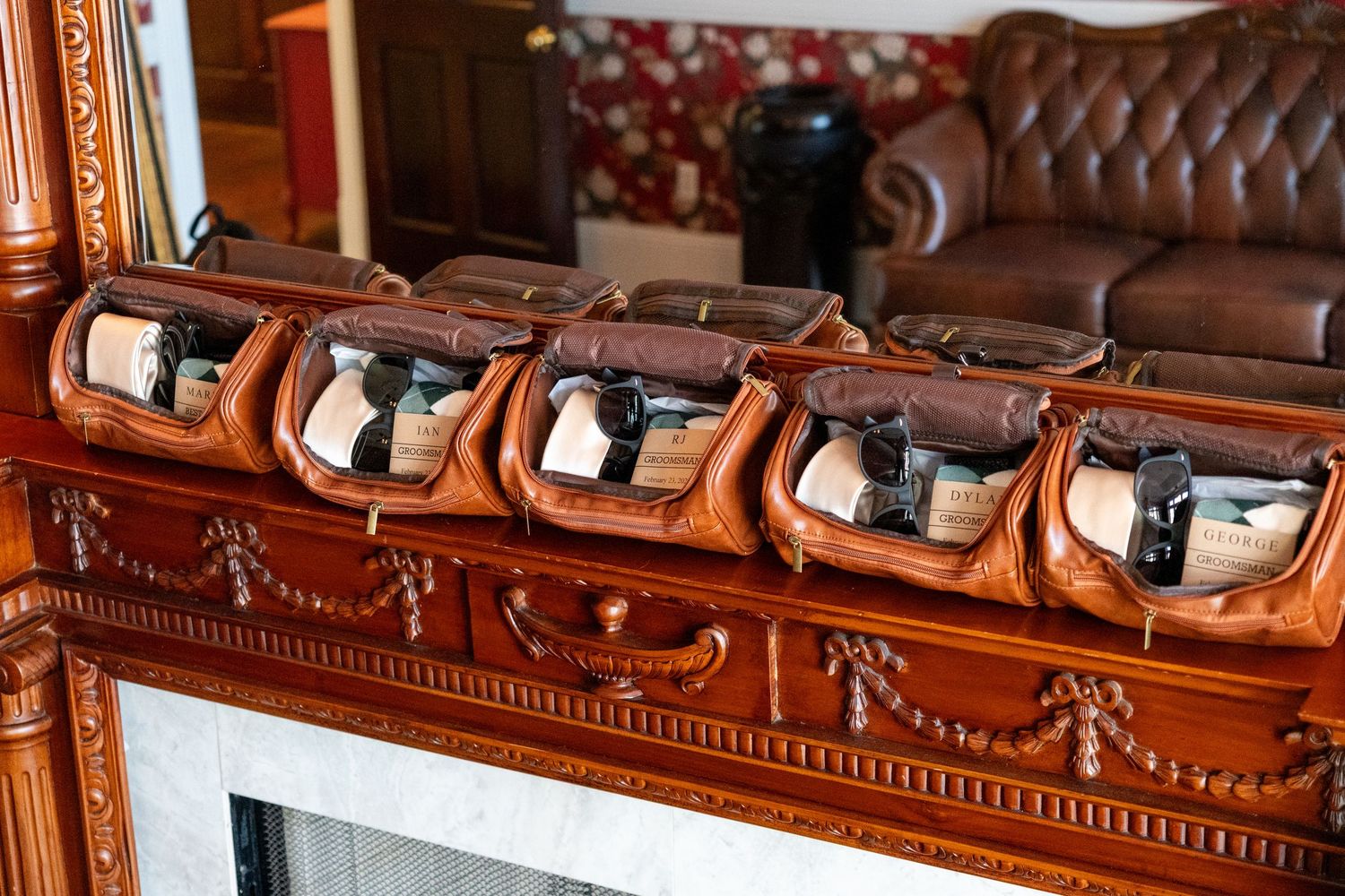 Elegant wooden fireplace mantel displaying multiple leather bags with handguns in an ornate living room setting.