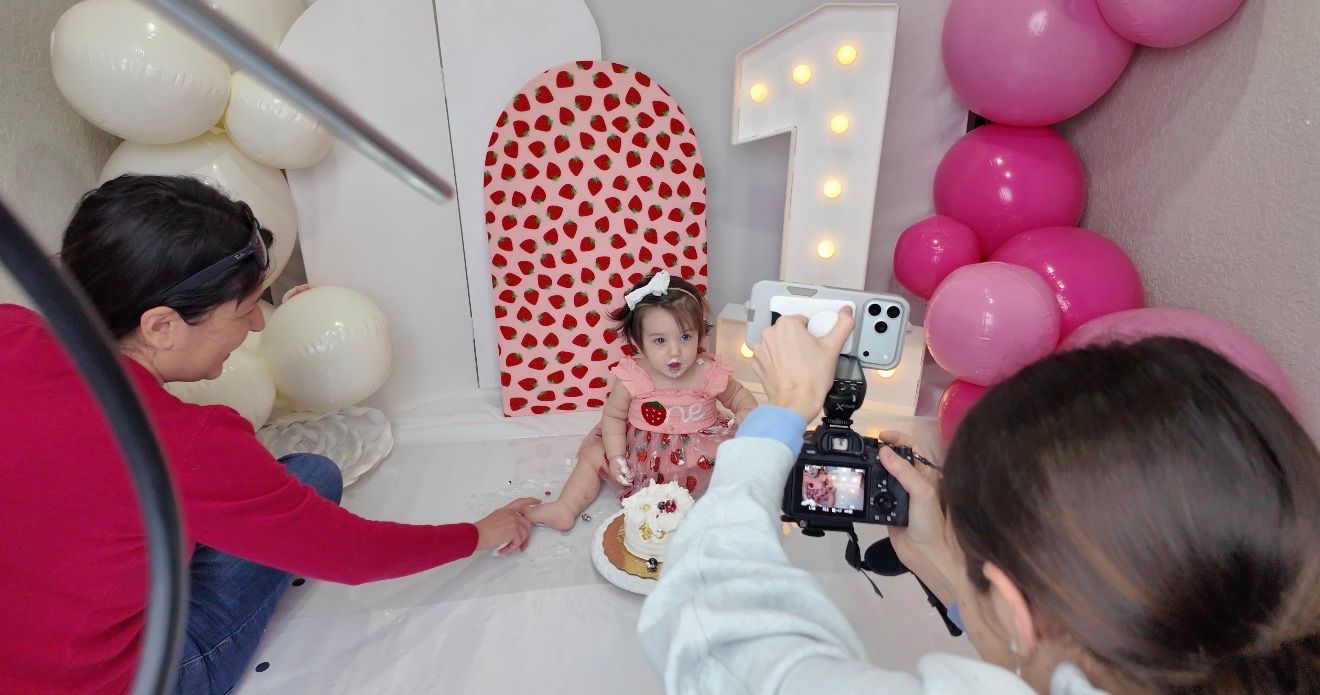Behind-the-scenes of a toddler's first birthday photoshoot with pink balloons and cake smash setup.
