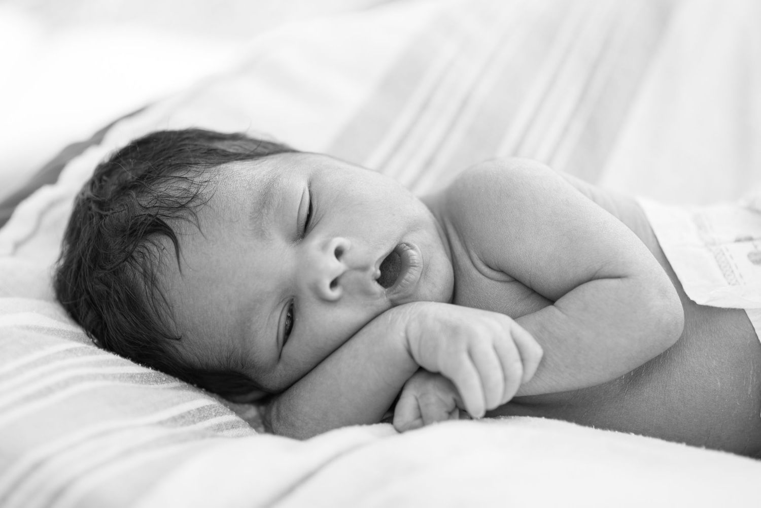 Black and white photo of a peaceful newborn baby sleeping on a soft white blanket.