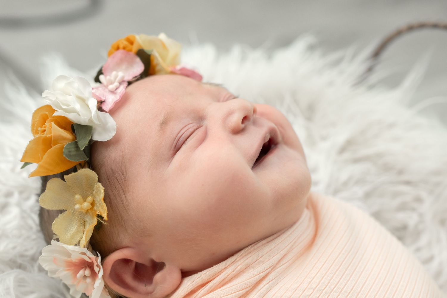 Newborn baby girl sleeping peacefully wrapped in peach swaddle wearing a delicate floral crown headband.