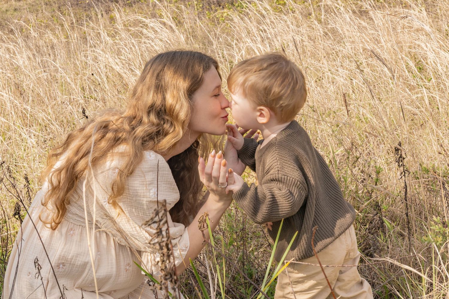 A mother and young boy share a tender nose-to-nose moment in a golden field of tall grass.