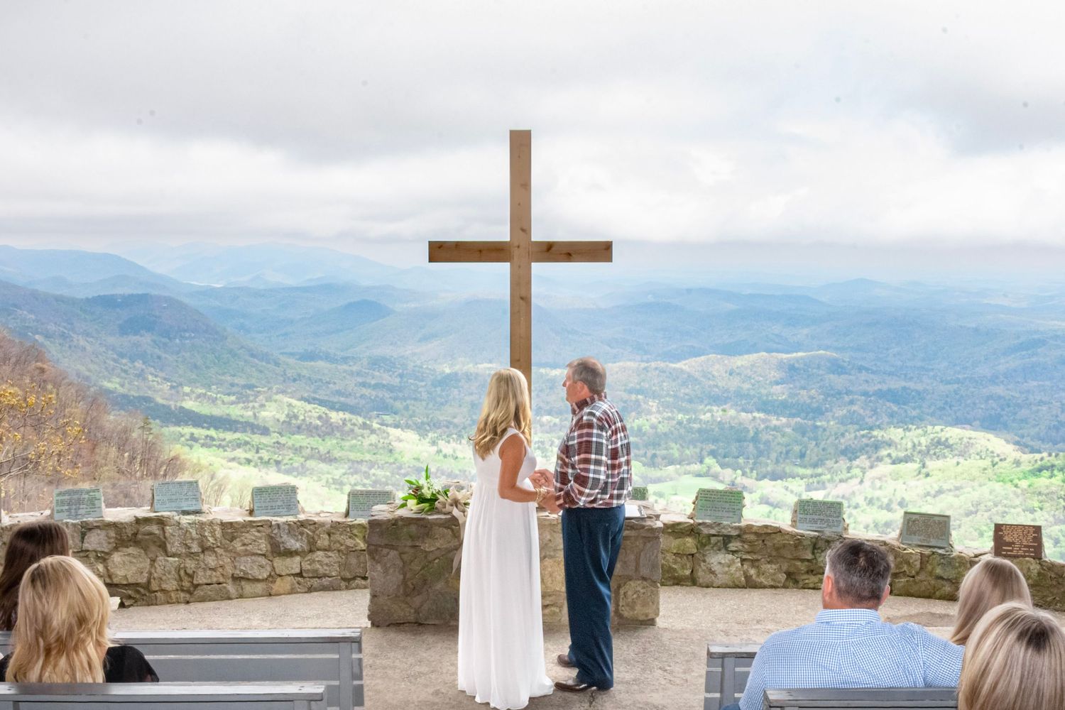 Couple exchanging vows before a wooden cross at a mountain overlook wedding ceremony with scenic valley views.