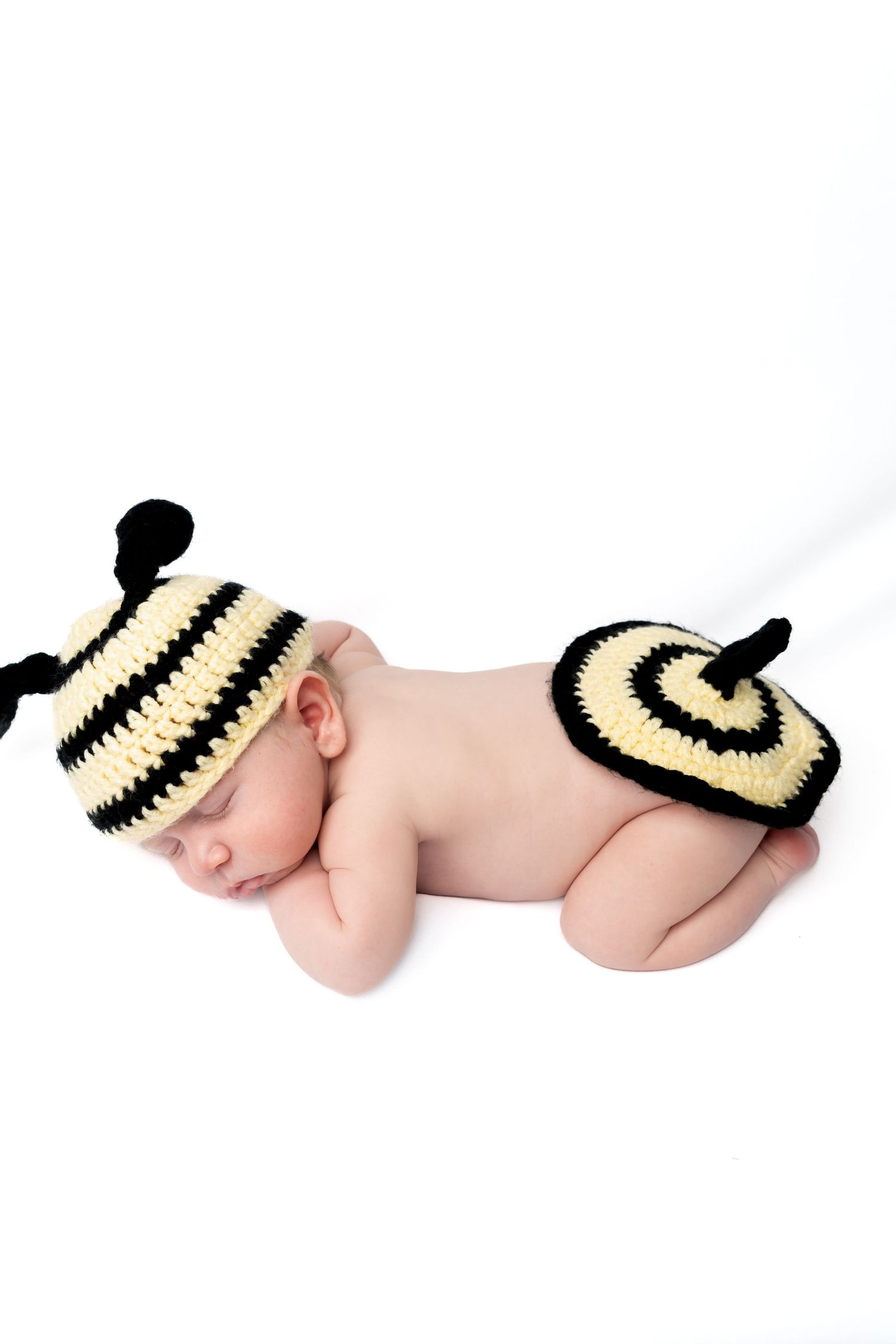 Sleeping newborn baby wearing a cute crocheted black and yellow bumblebee hat and diaper cover costume.