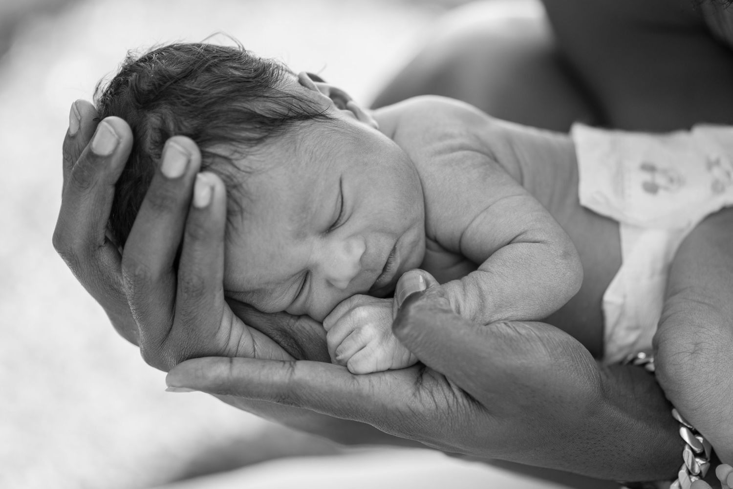Black and white photo of a sleeping newborn baby cradled gently in adult hands.
