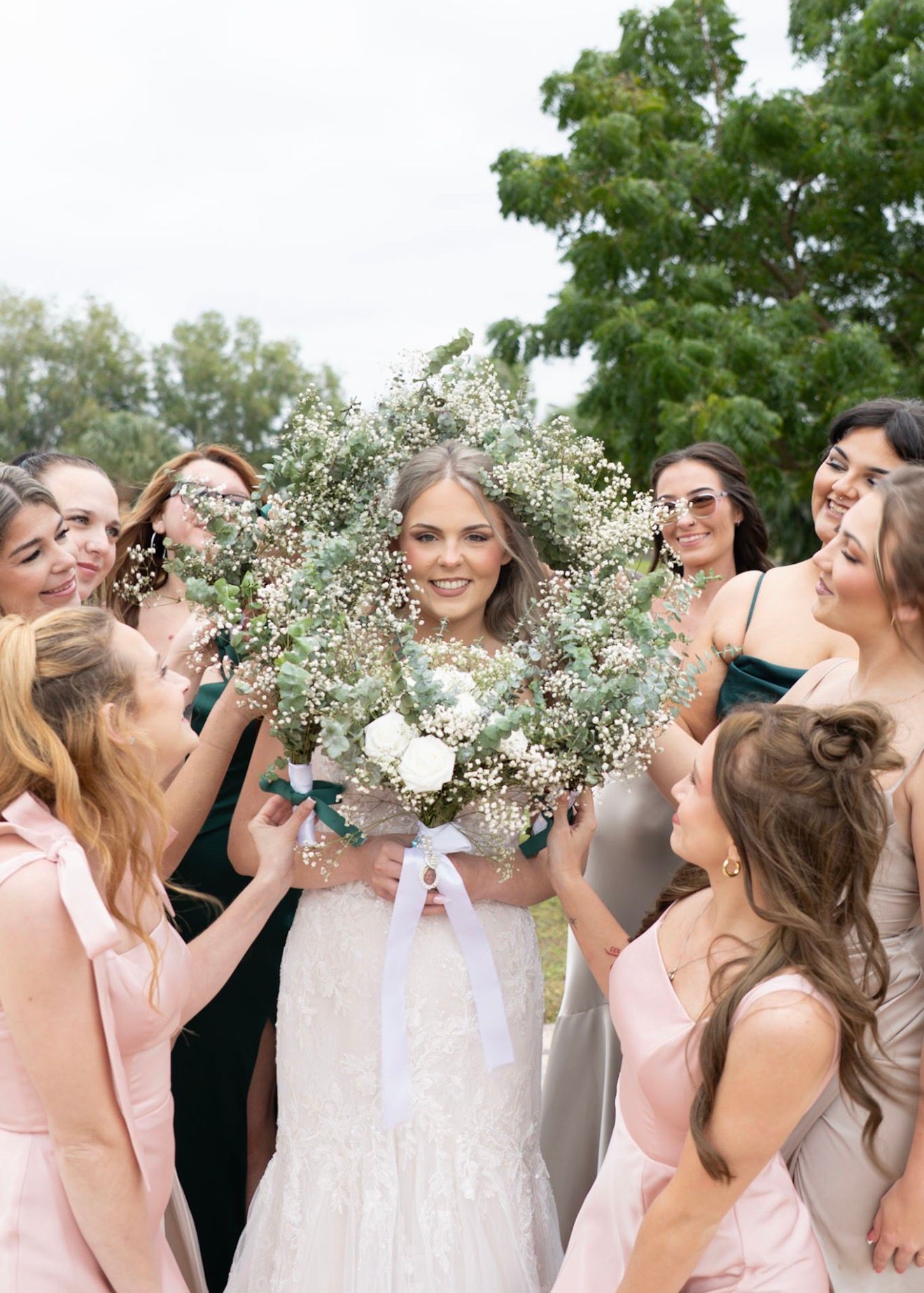 Smiling bride surrounded by bridesmaids holding large baby's breath bouquet.