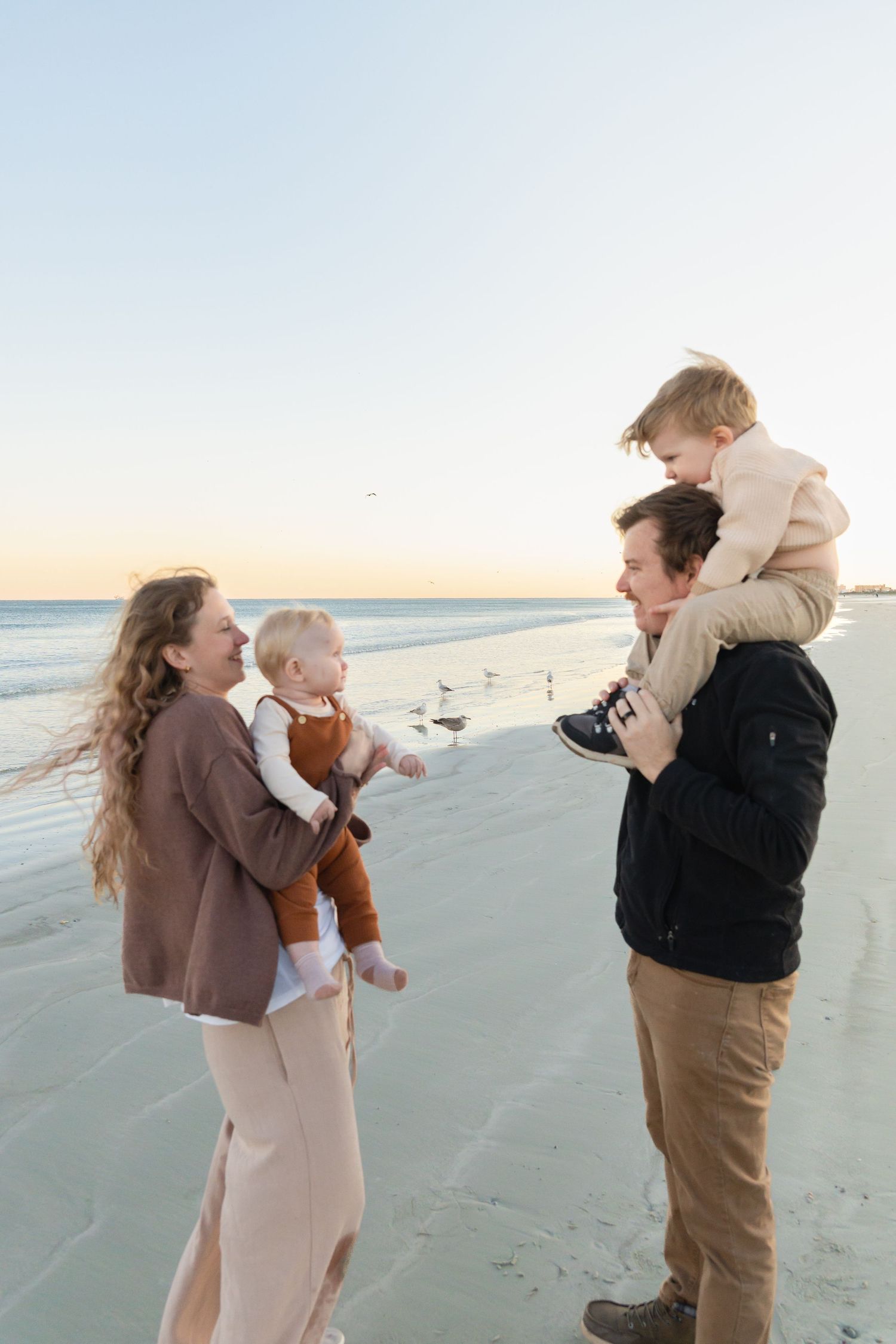 Happy family of four enjoying a beautiful sunset beach walk, parents carrying young children.