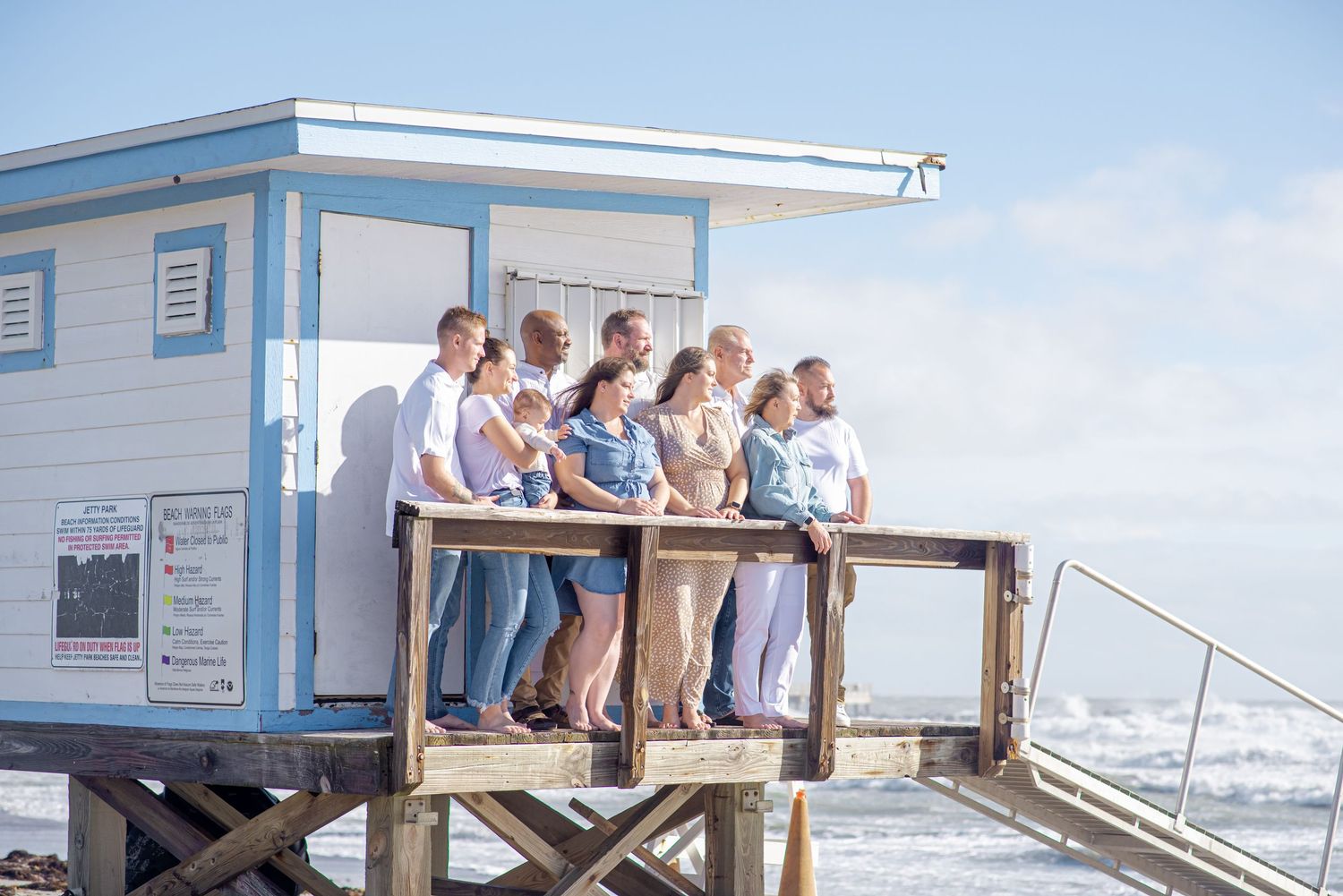 Group of people posing together on a beach lifeguard tower deck with ocean waves in the background.