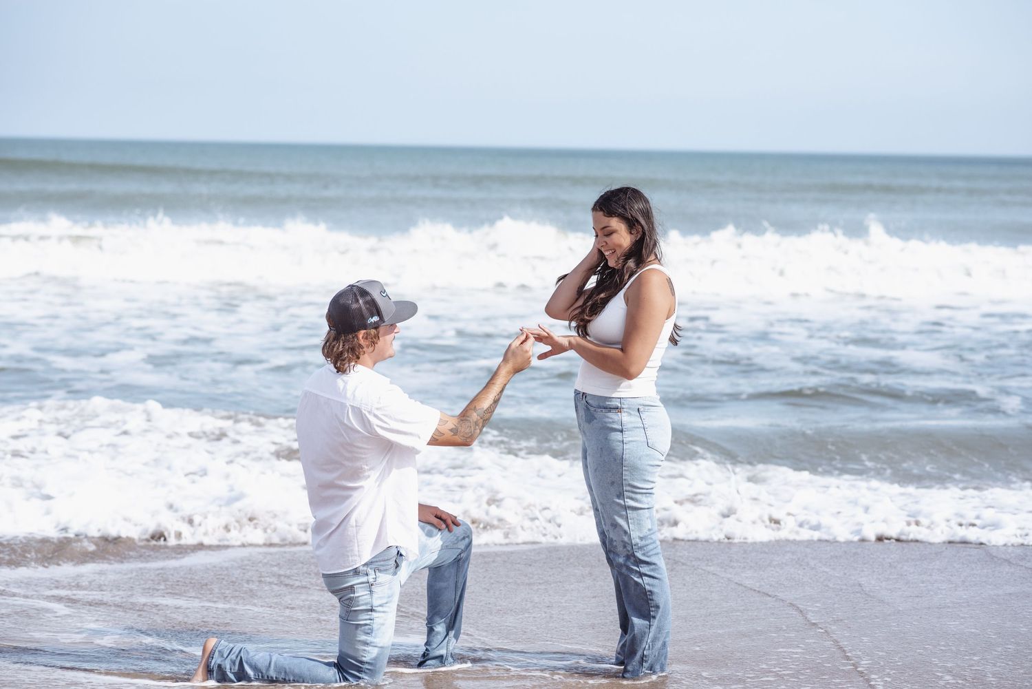 A romantic beach proposal with a person kneeling on one knee offering a ring to their partner by the ocean waves.