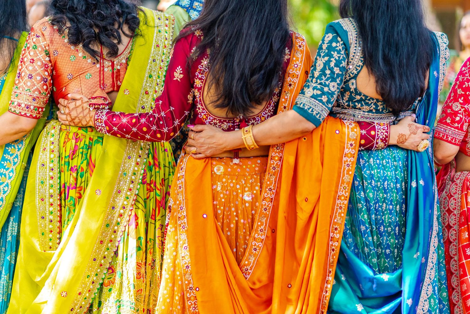 Group of women in colorful Indian sarees standing together with arms around each other at a festive celebration.