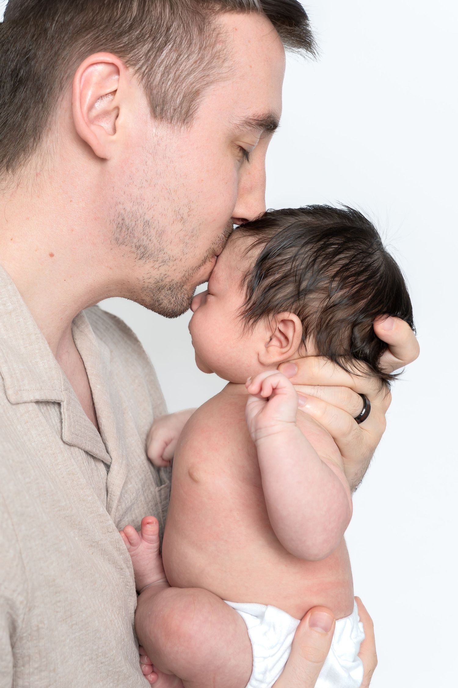 Father tenderly kisses his newborn baby on the forehead while cradling the infant against his chest.