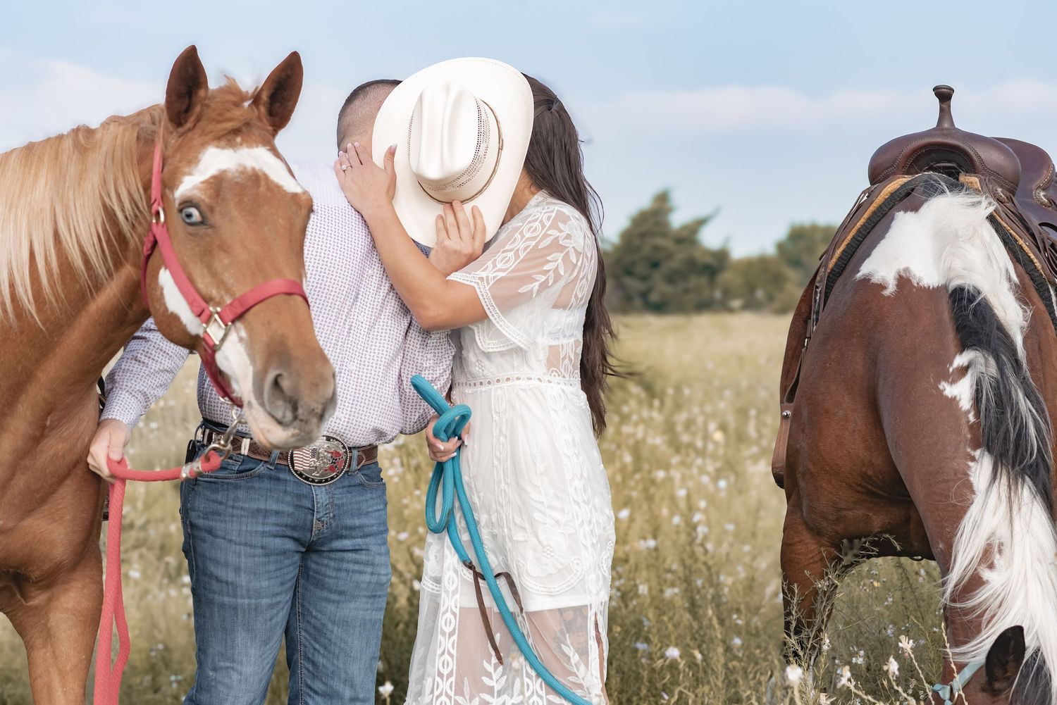 Couple sharing romantic kiss between two horses in a meadow.