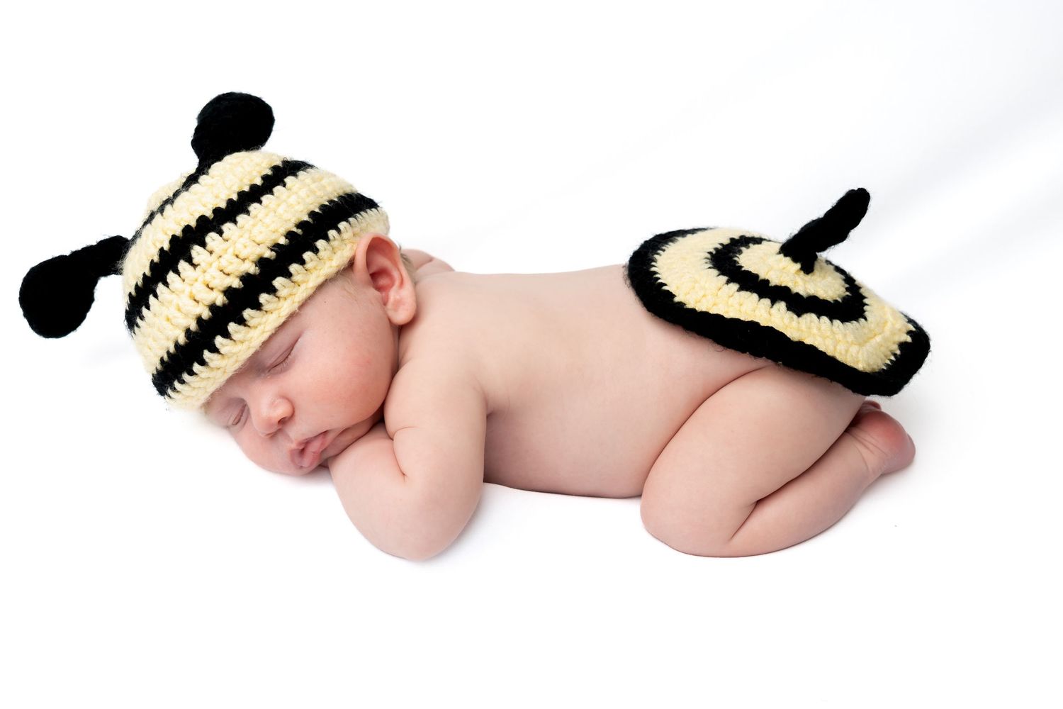 Sleeping newborn baby wearing a crocheted black and yellow bumblebee hat and diaper cover costume.