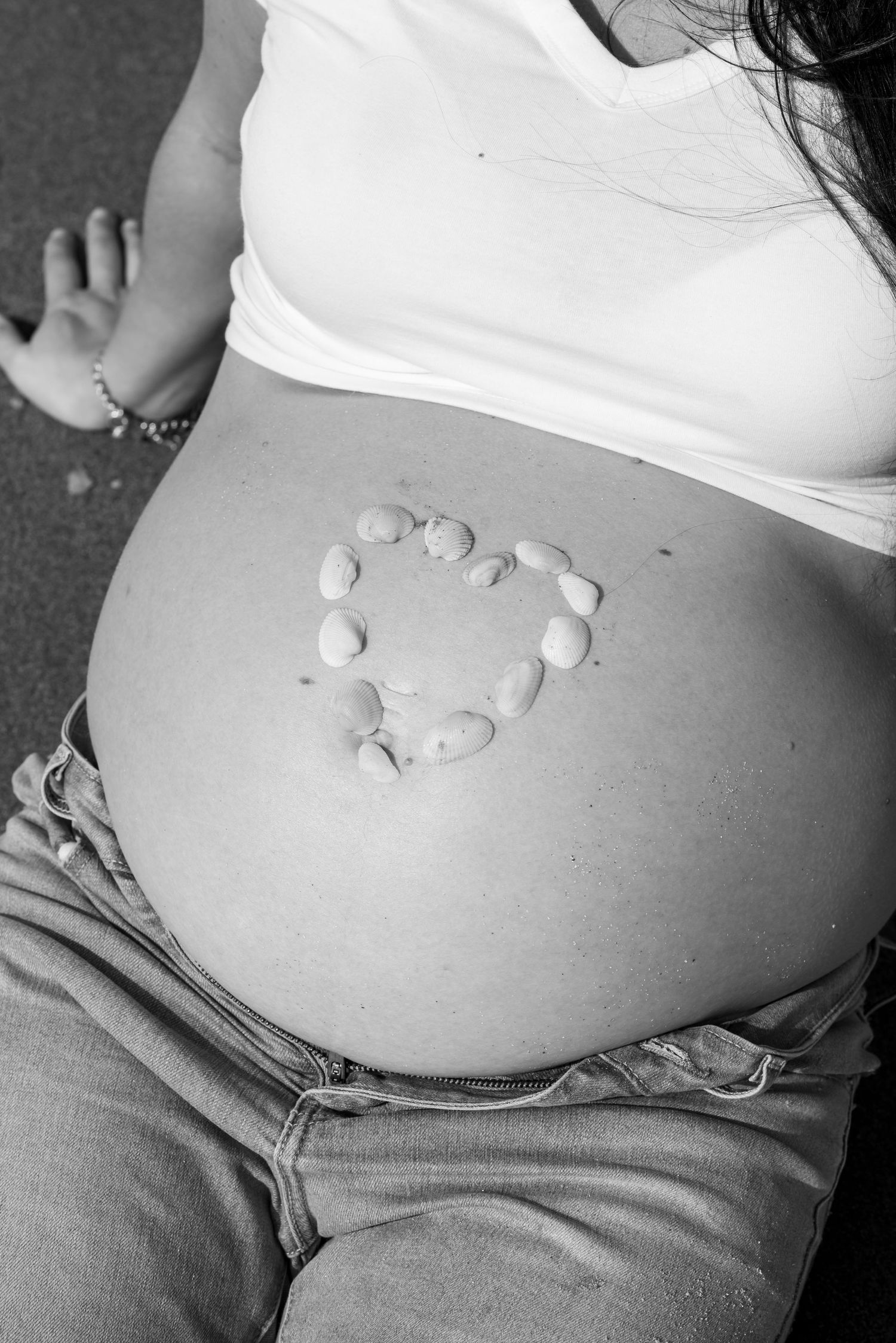 Black and white photo of pregnant woman's bare belly with small stones arranged in a heart shape on her bump.