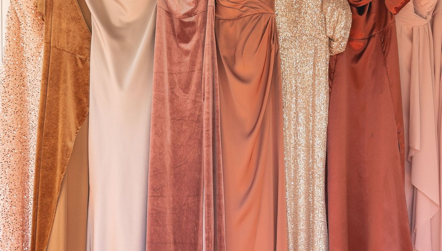 A row of elegant bridesmaid dresses in blush, rose, and terracotta tones hanging on a rack.