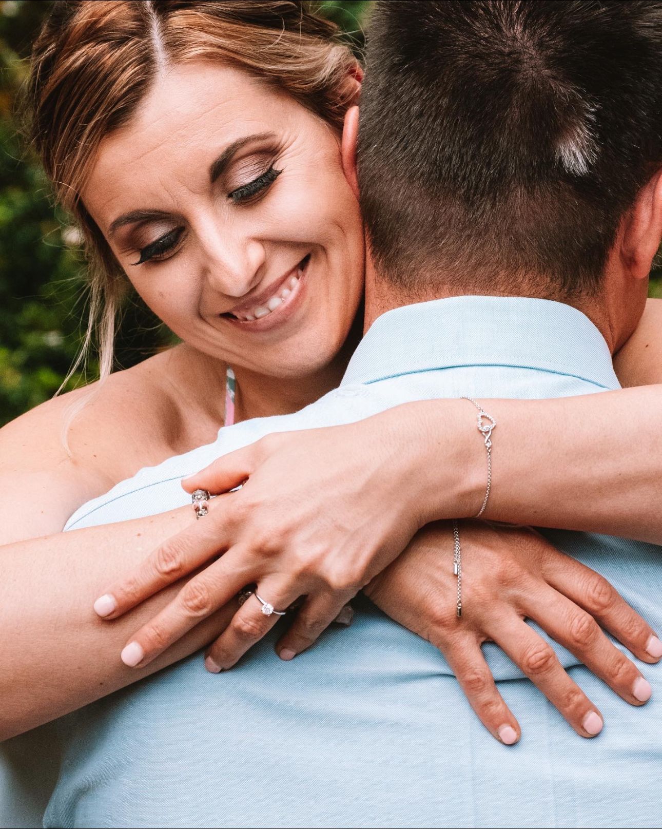 Smiling bride hugging groom, showing engagement ring and delicate bracelet during romantic wedding moment.