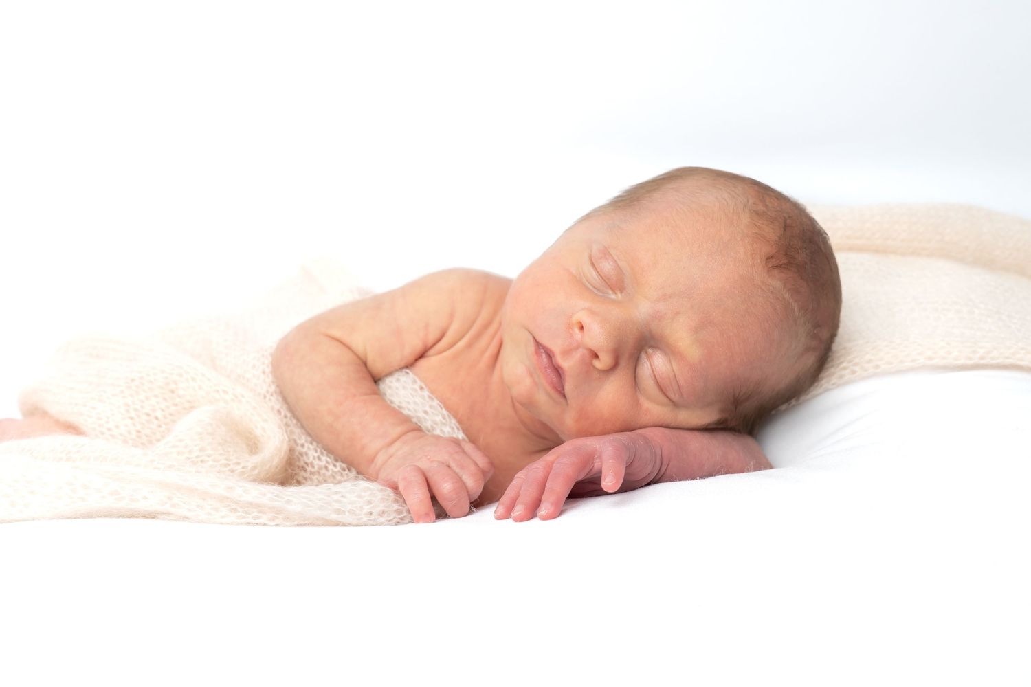 Peaceful newborn baby sleeping on white blanket with soft pink wrap, serene infant portrait photography.