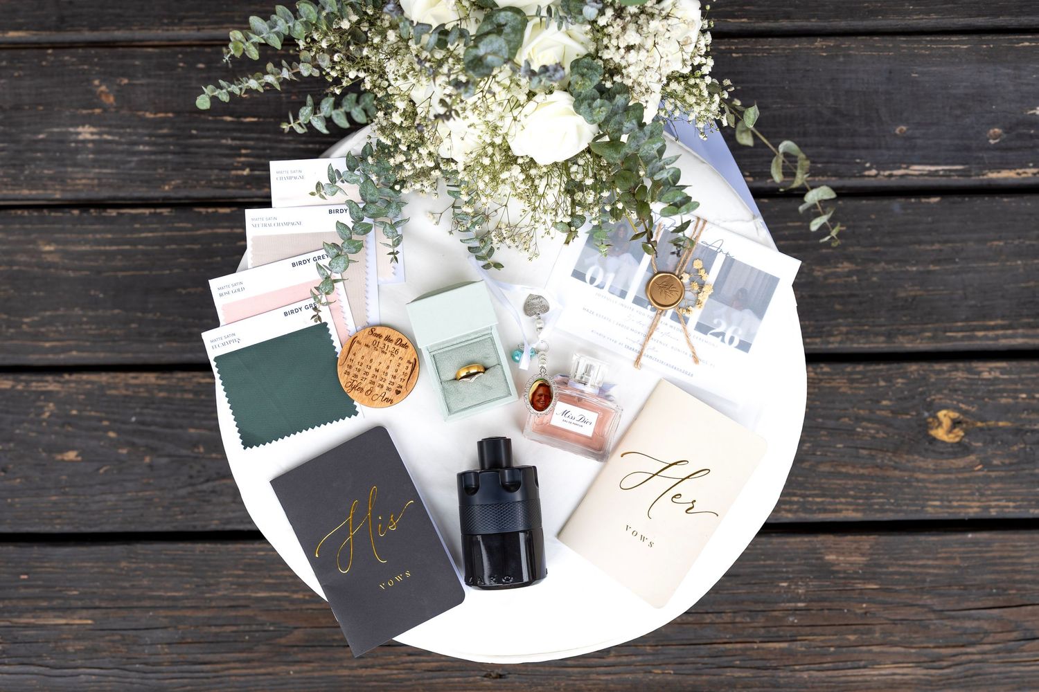 Elegant wedding flat lay with floral bouquet, perfume, rings, and personalized stationery on a white round tray.