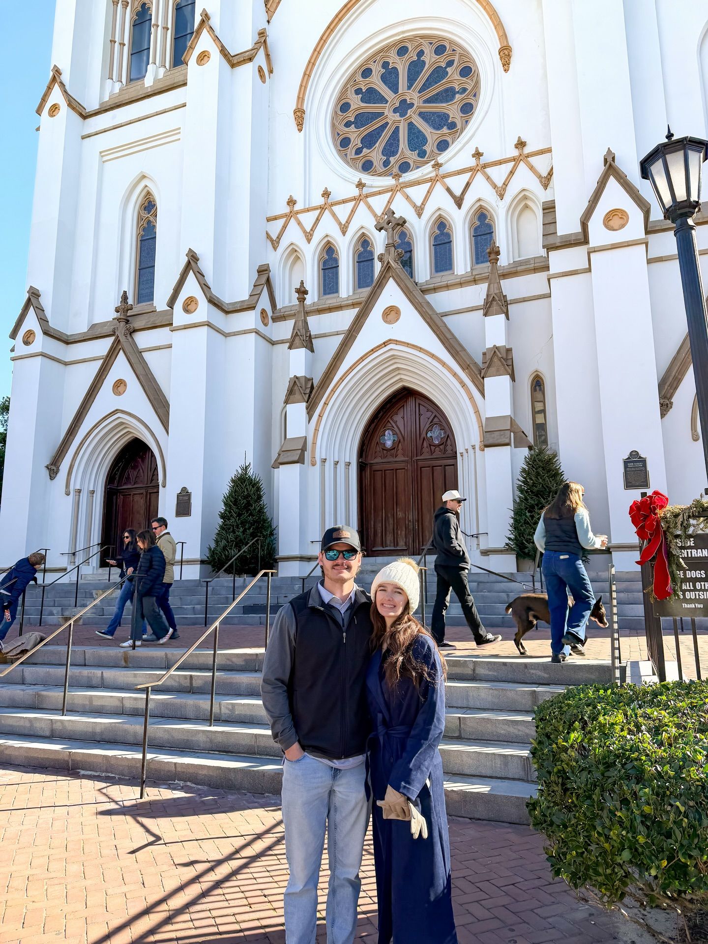 Couple posing in front of white Gothic cathedral with rose window on sunny winter day.