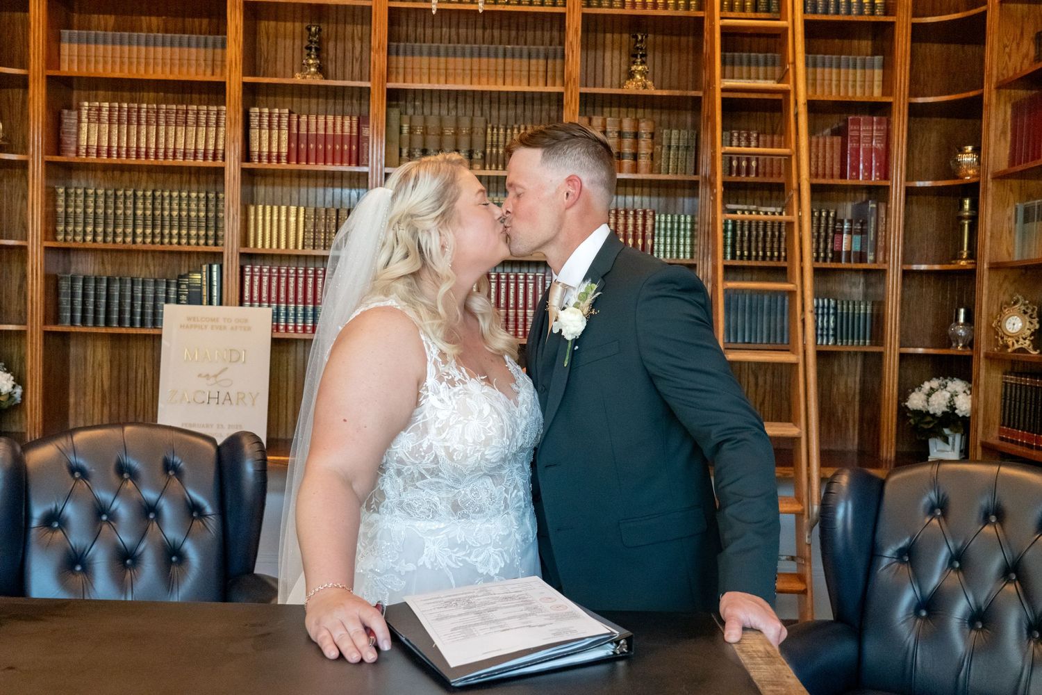 Bride and groom share a romantic kiss in an elegant library setting after signing wedding registry.
