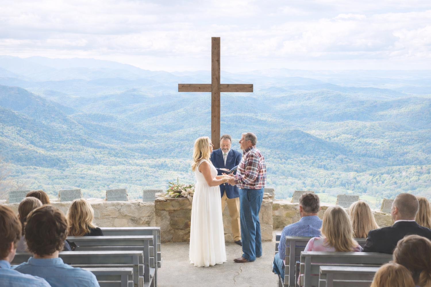 Couple exchanging wedding vows at an outdoor mountain ceremony with a large cross and scenic views.