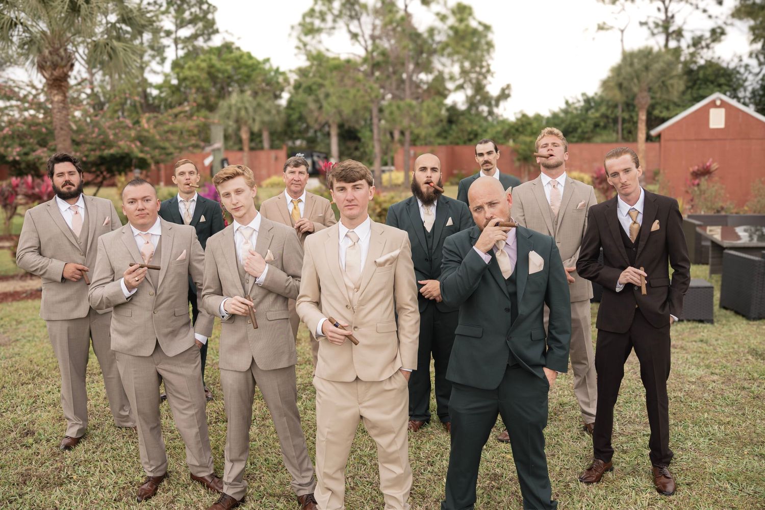Groomsmen in tan and dark suits posing outdoors before a wedding ceremony.