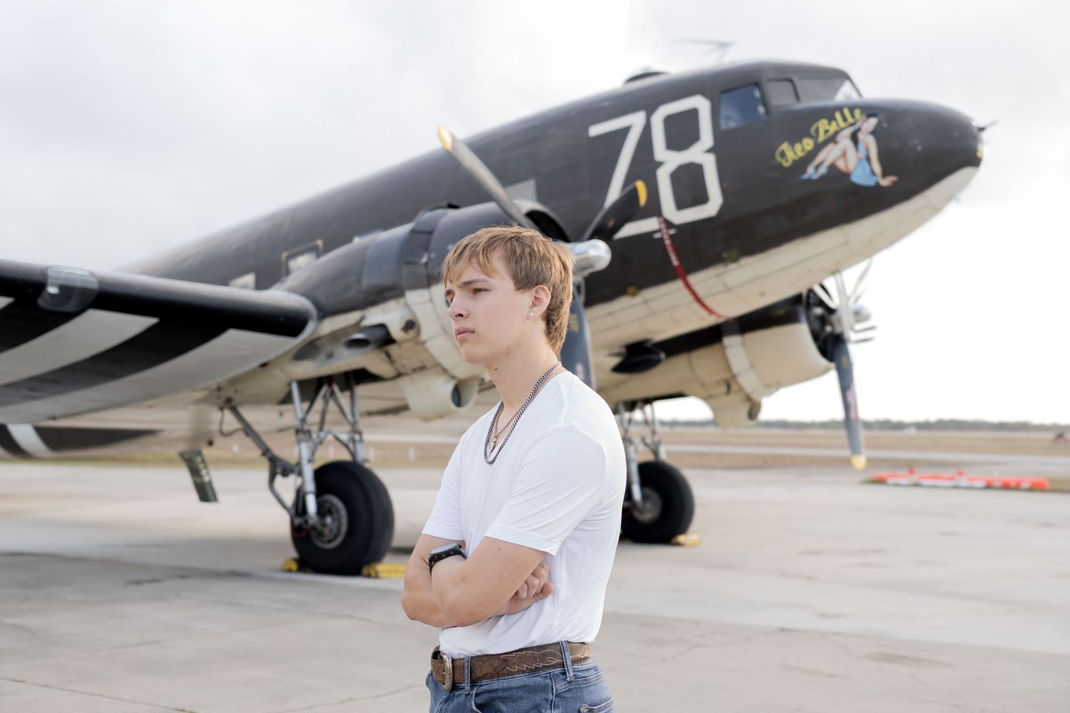 Young man with arms crossed standing in front of a vintage military aircraft numbered 78.