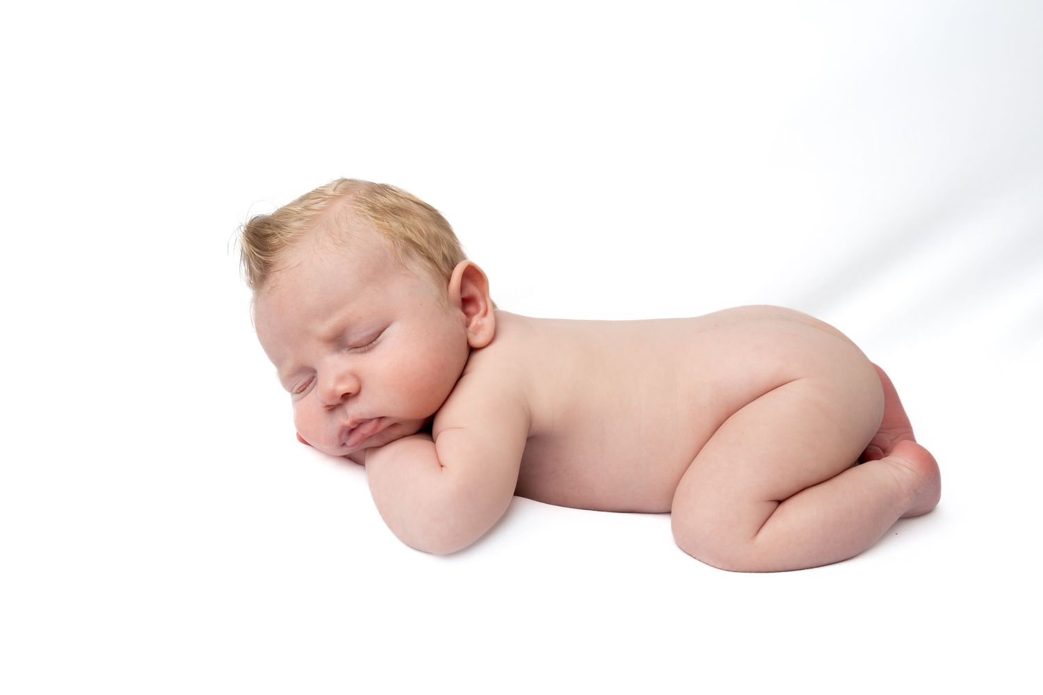 Peaceful newborn baby sleeping curled up on white background in classic newborn photography pose.