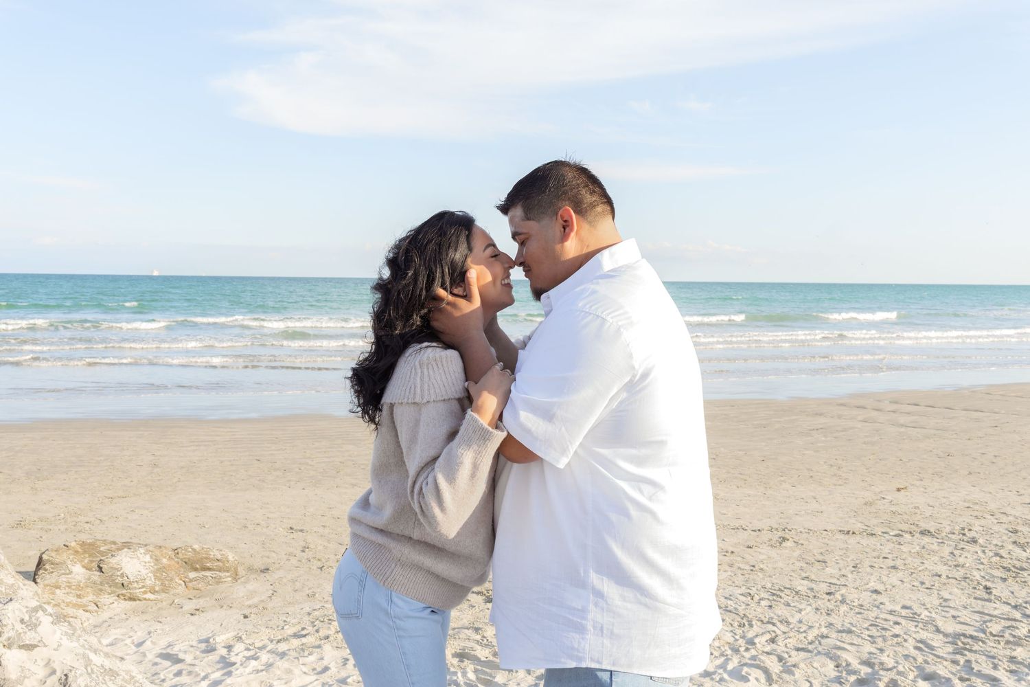 Couple sharing a romantic moment on a sandy beach with ocean waves in the background.