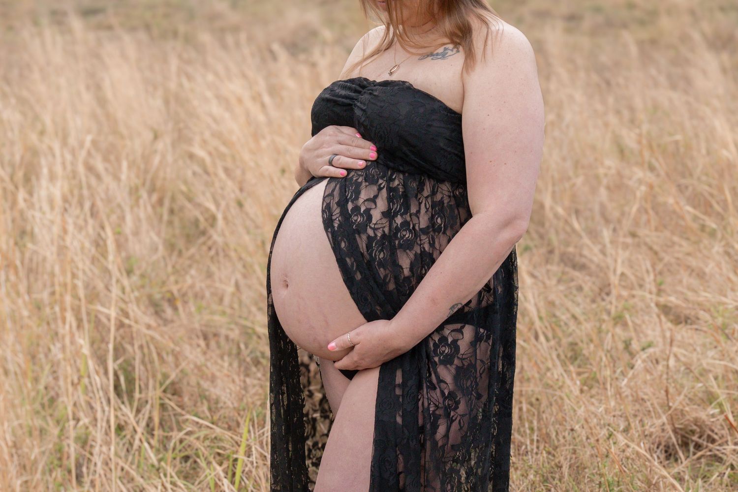 Pregnant woman in black lace dress cradling baby bump in golden field.