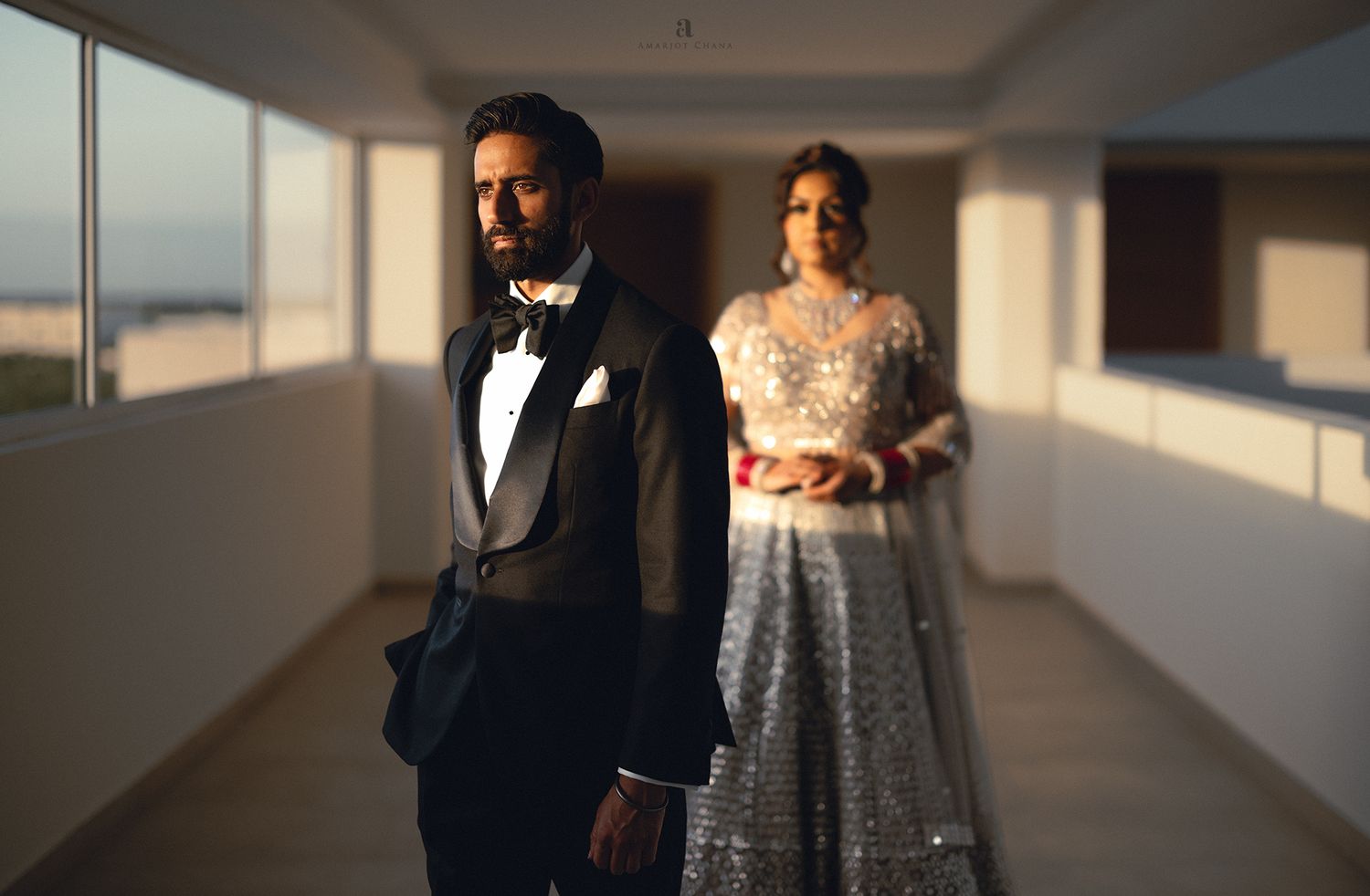 Mexico Indian wedding – groom in black tuxedo and bride in silver lehenga posing in dramatic corridor lighting, modern Indian wedding
