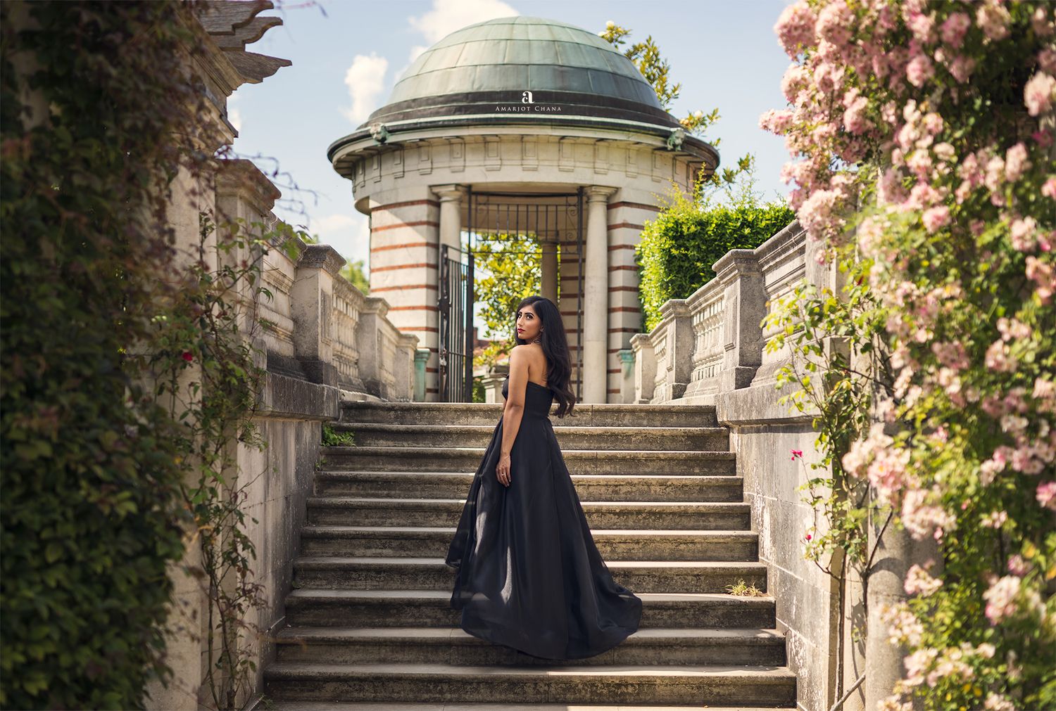 Kabir and Kevita pre-wedding portraits – woman in dramatic black gown posing on stone steps surrounded by blooming roses near grand rotunda,