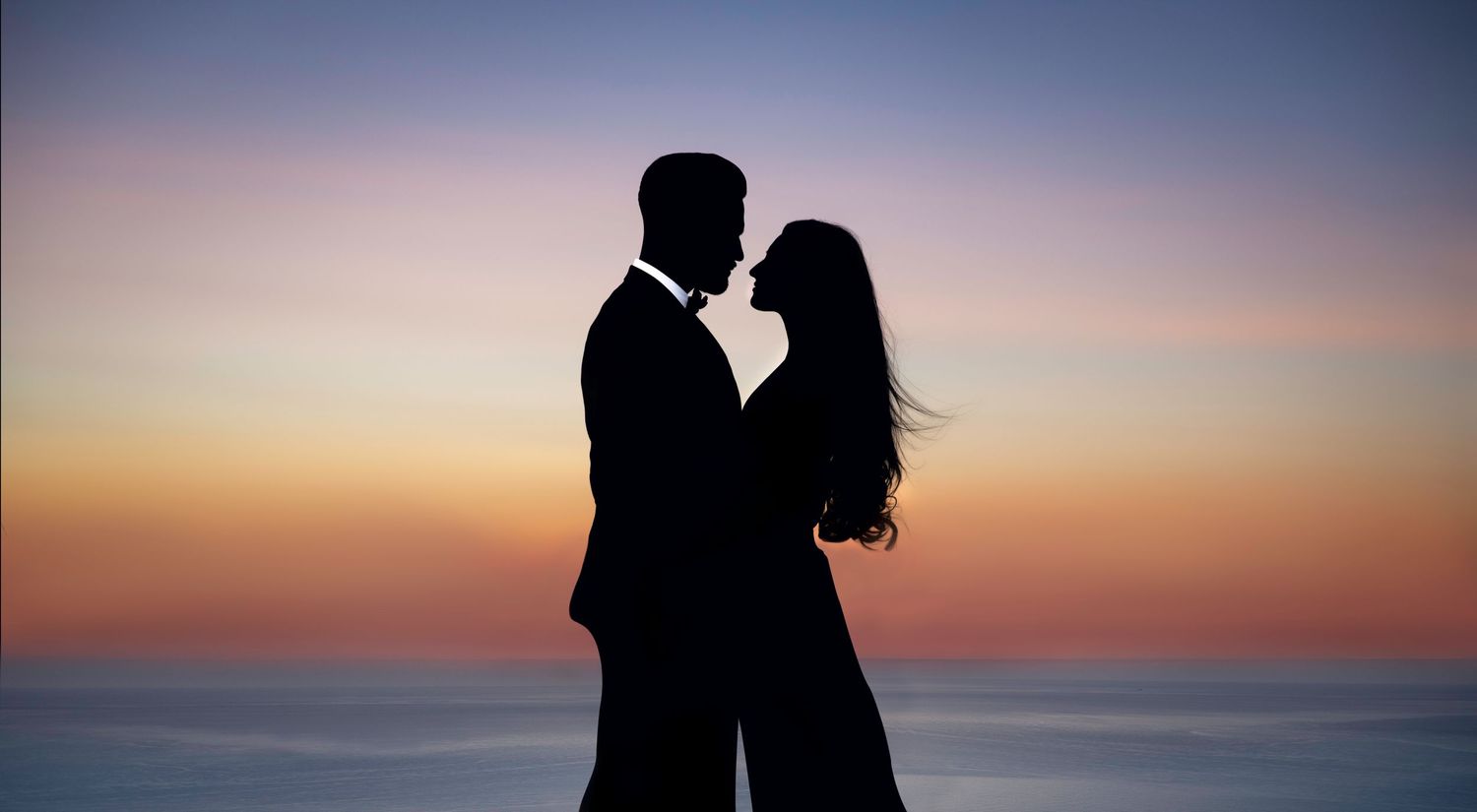 Pre-wedding portraits – romantic couple silhouette kissing against vibrant purple orange sunset sky, cinematic Indian wedding photography