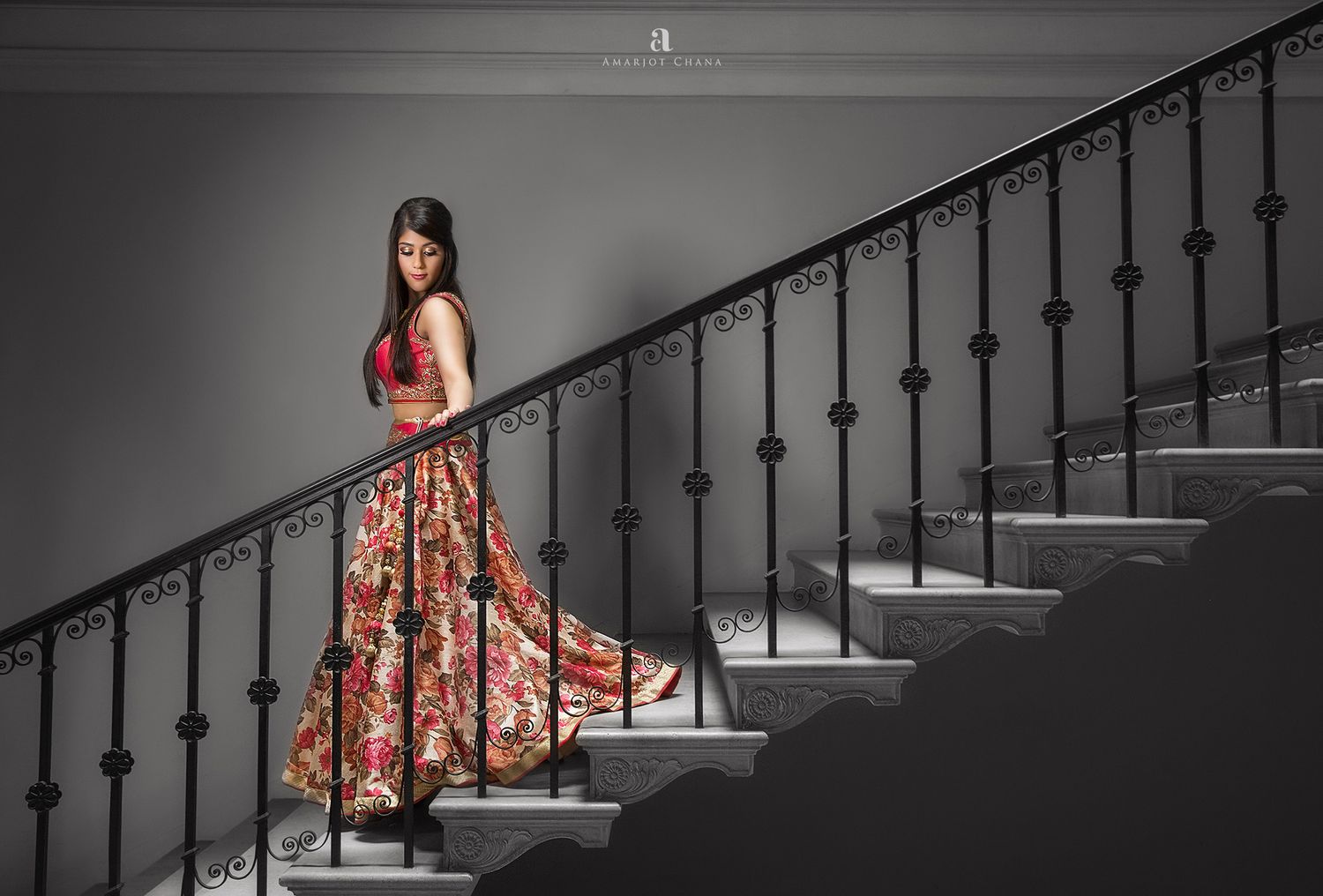 Jon and Jessica wedding – bride in vibrant colourful floral lehenga posing elegantly on grand staircase in dramatic black and white setting,