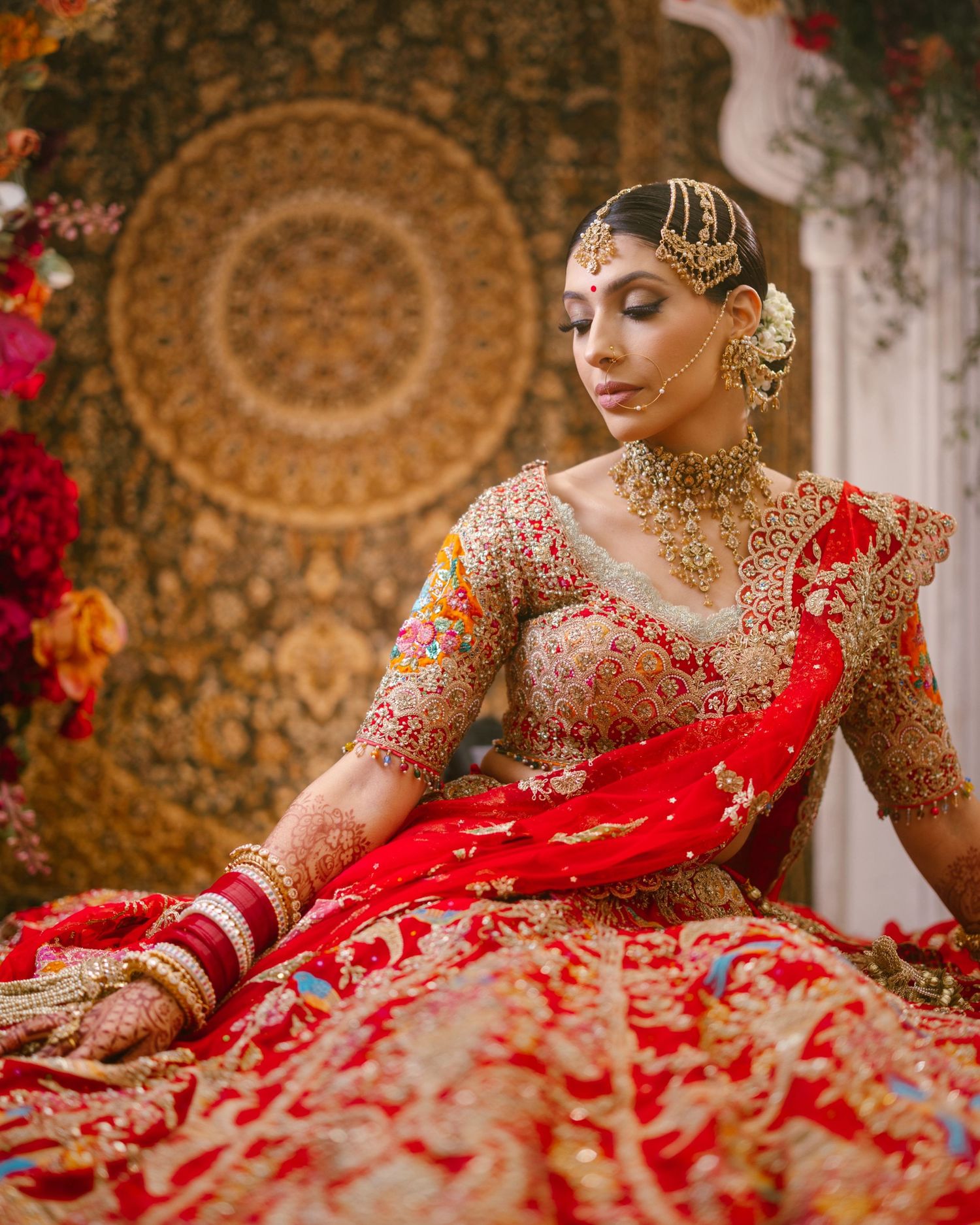 Indian bride seated in ornate red and gold bridal lehenga with kundan jewellery and gold hairpiece, Sikh Hindu wedding photography by Amarjo