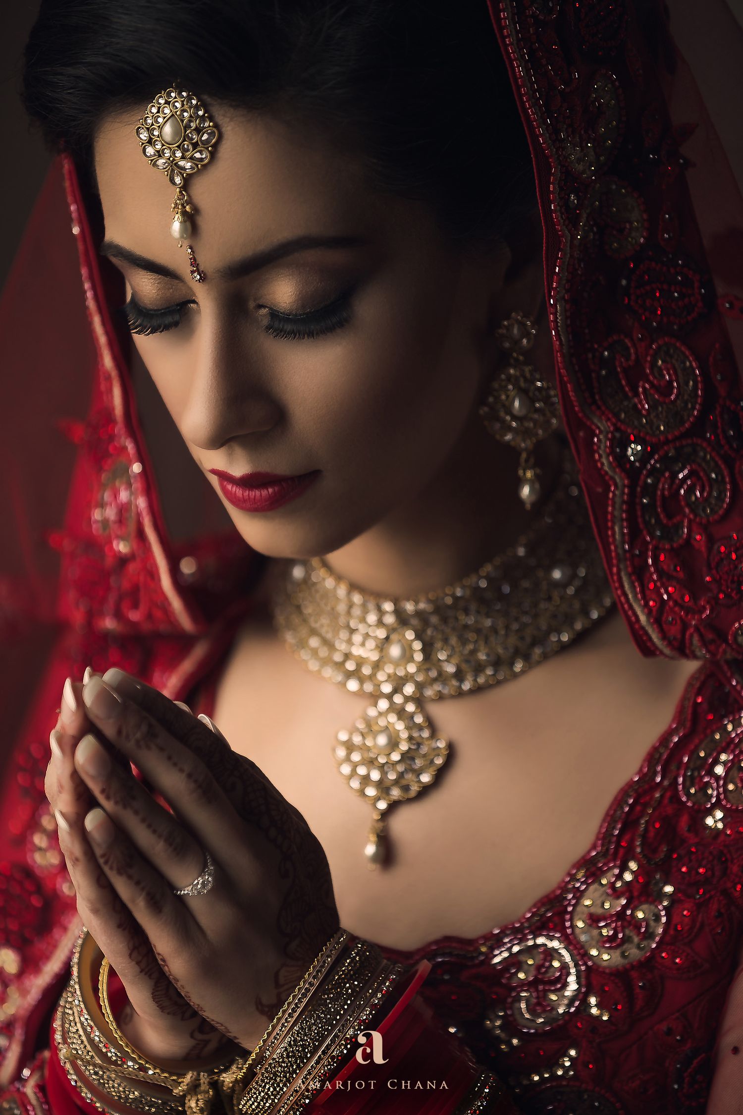 Indian bride in red lehenga with gold jewellery praying with folded hands, devotional moment captured at Indian wedding by Amarjot Chana